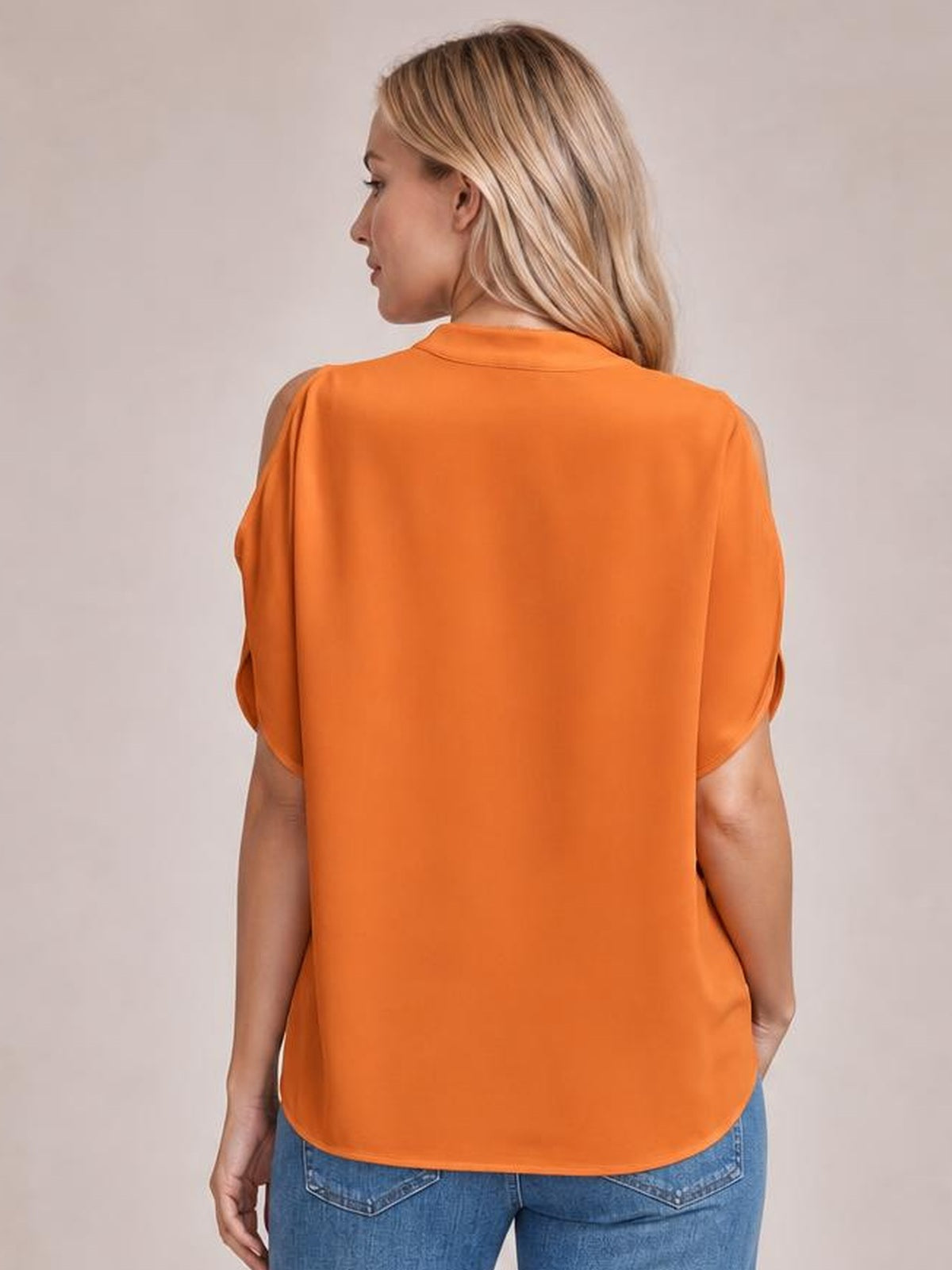 A model looks over her shoulder wearing an orange Notched Cold Shoulder Blouse with exposed shoulders, short sleeves, a relaxed silhouette, and rounded hem.