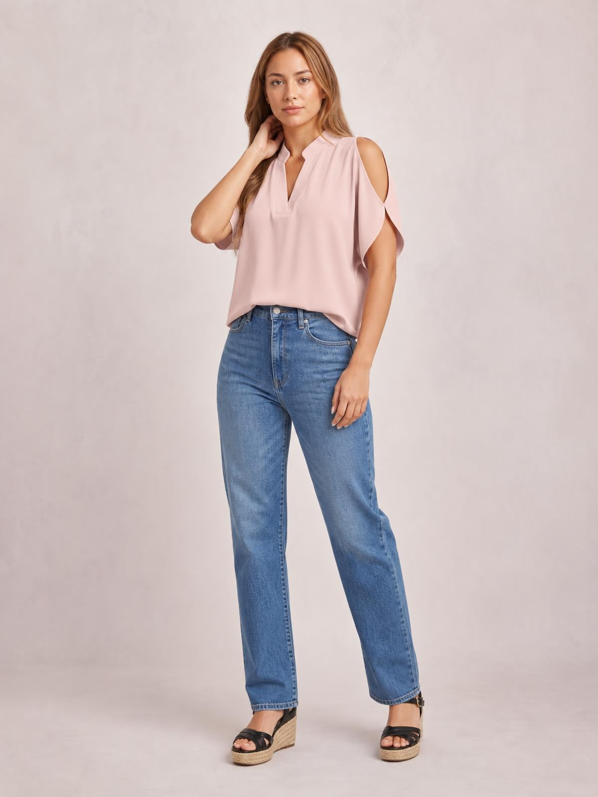 A model poses in a blush pink notched cold shoulder blouse with flowing short sleeves, shoulder cutouts, a relaxed straight silhouette, and a loose hem.