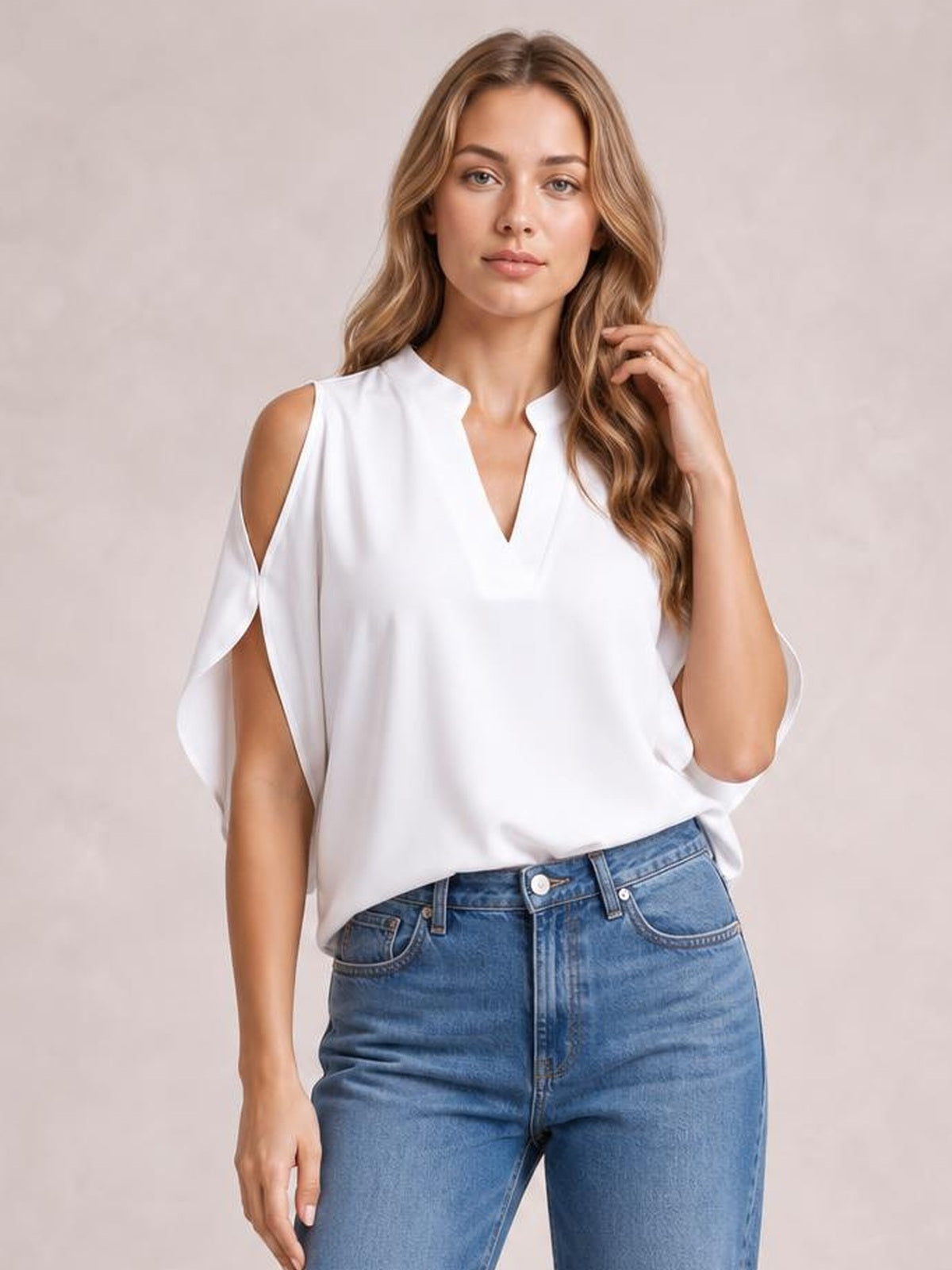 Model wearing a white notched cold shoulder blouse with a relaxed straight silhouette and draped cutout sleeves, paired with blue jeans.