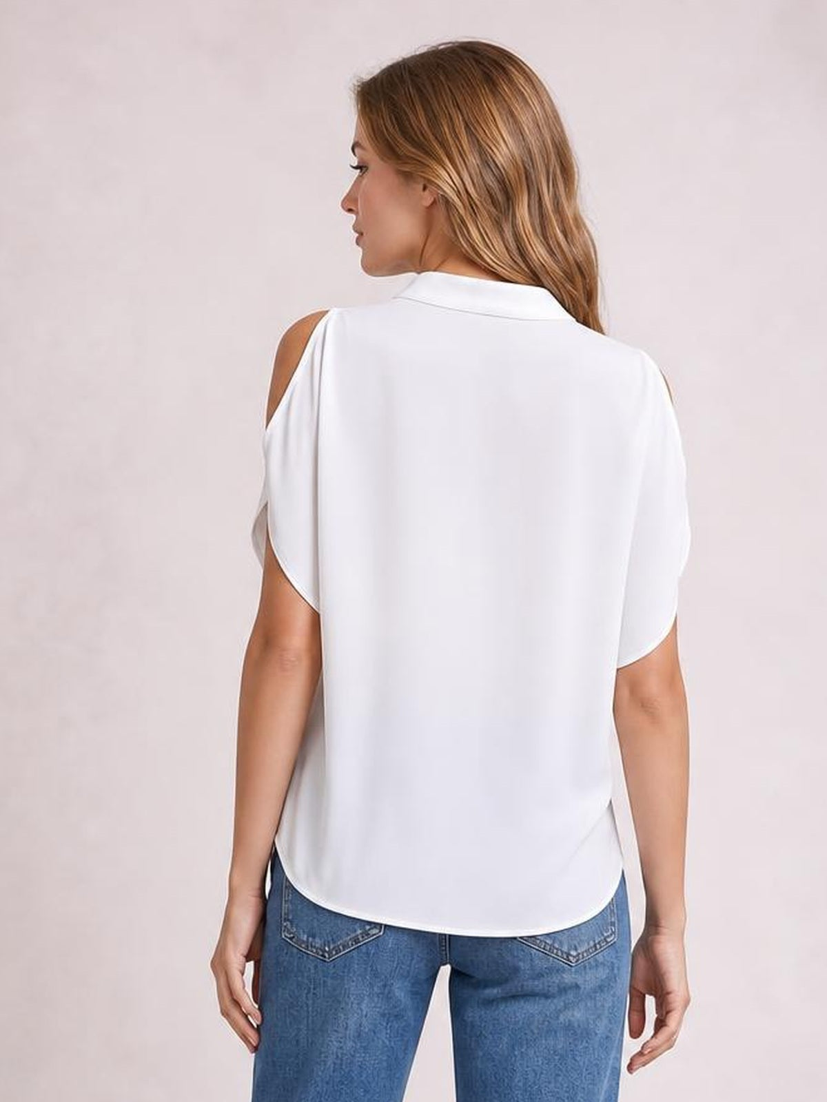 Back view of a model wearing a white notched cold shoulder blouse with a collared neckline, relaxed silhouette, short sleeves, and a curved hem.
