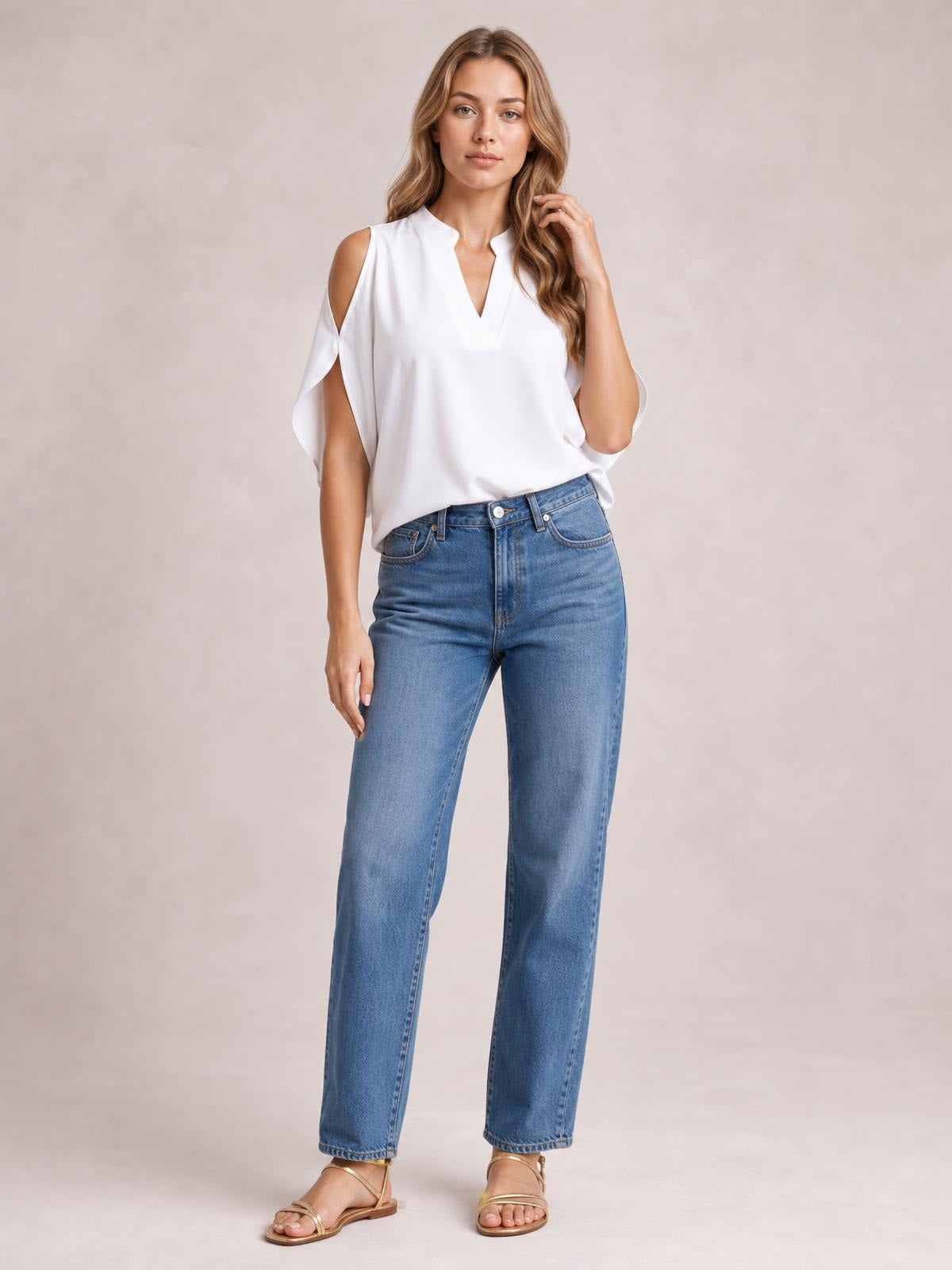 Model wearing a white notched cold shoulder blouse with a V-neckline, draped short sleeves, relaxed silhouette, and one hand touching her hair.
