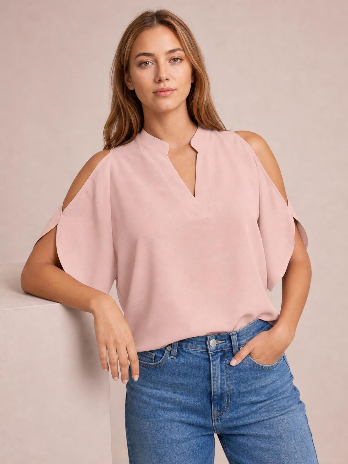 A model poses in a blush pink blouse with a notched neckline, cold-shoulder cutouts, flowing half sleeves, and a relaxed silhouette.