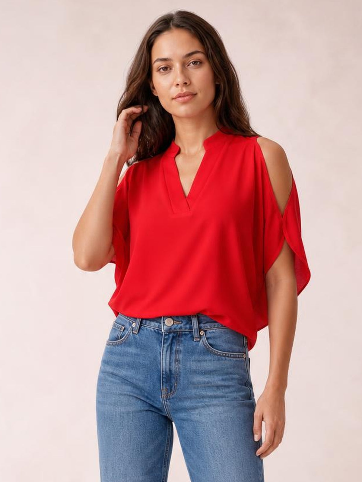 A model poses in a bright red notched cold shoulder blouse with a V neckline, flowing half sleeves, and a relaxed silhouette, touching her hair.