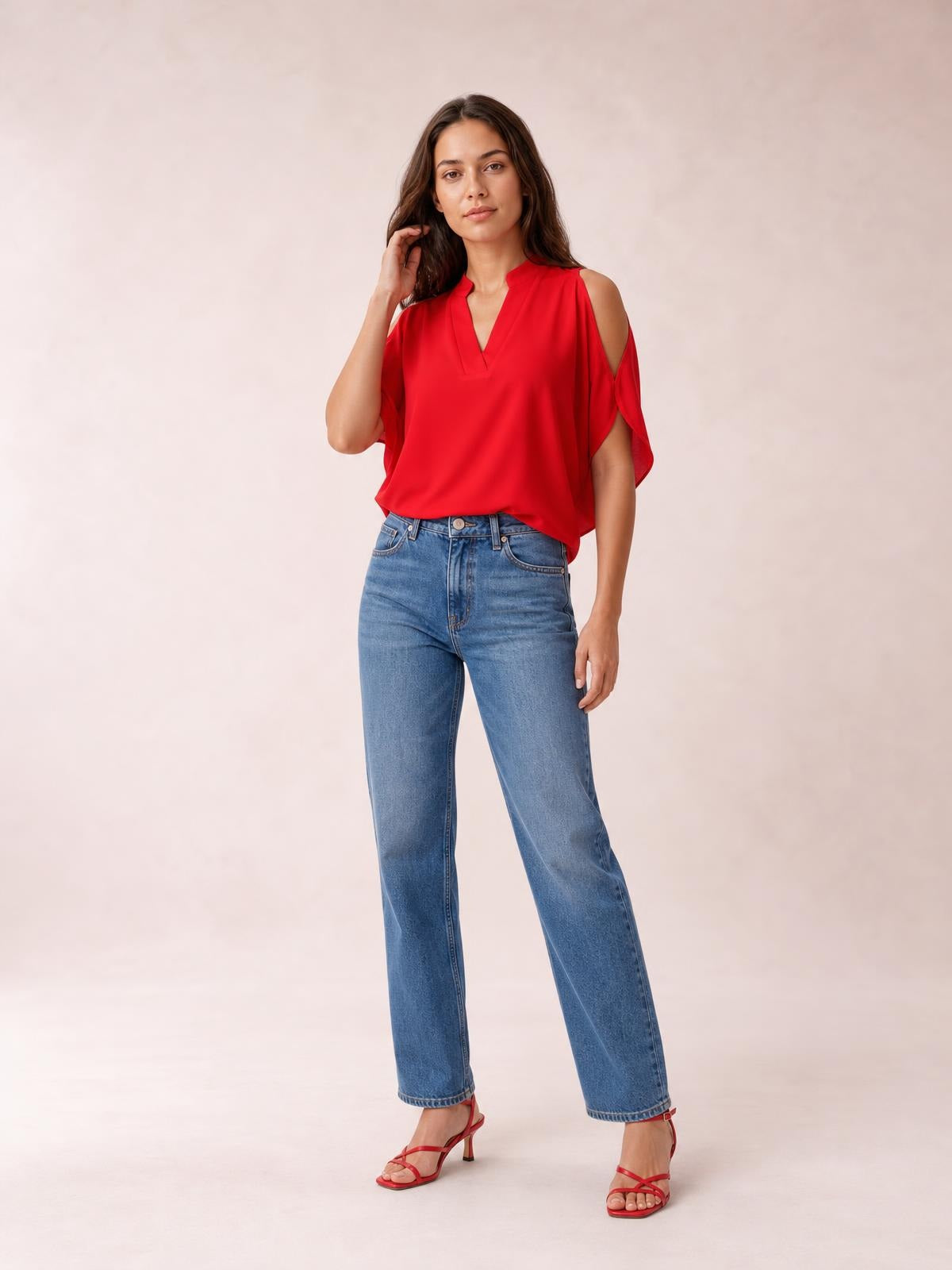 A model poses in a red notched cold shoulder blouse with half sleeves, an airy relaxed silhouette, and draped construction, paired with jeans.