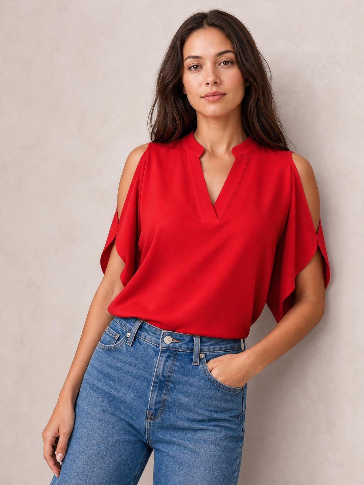 A model stands in a red notched cold shoulder blouse with half sleeves, open shoulder cutouts, a relaxed silhouette, and blue jeans.