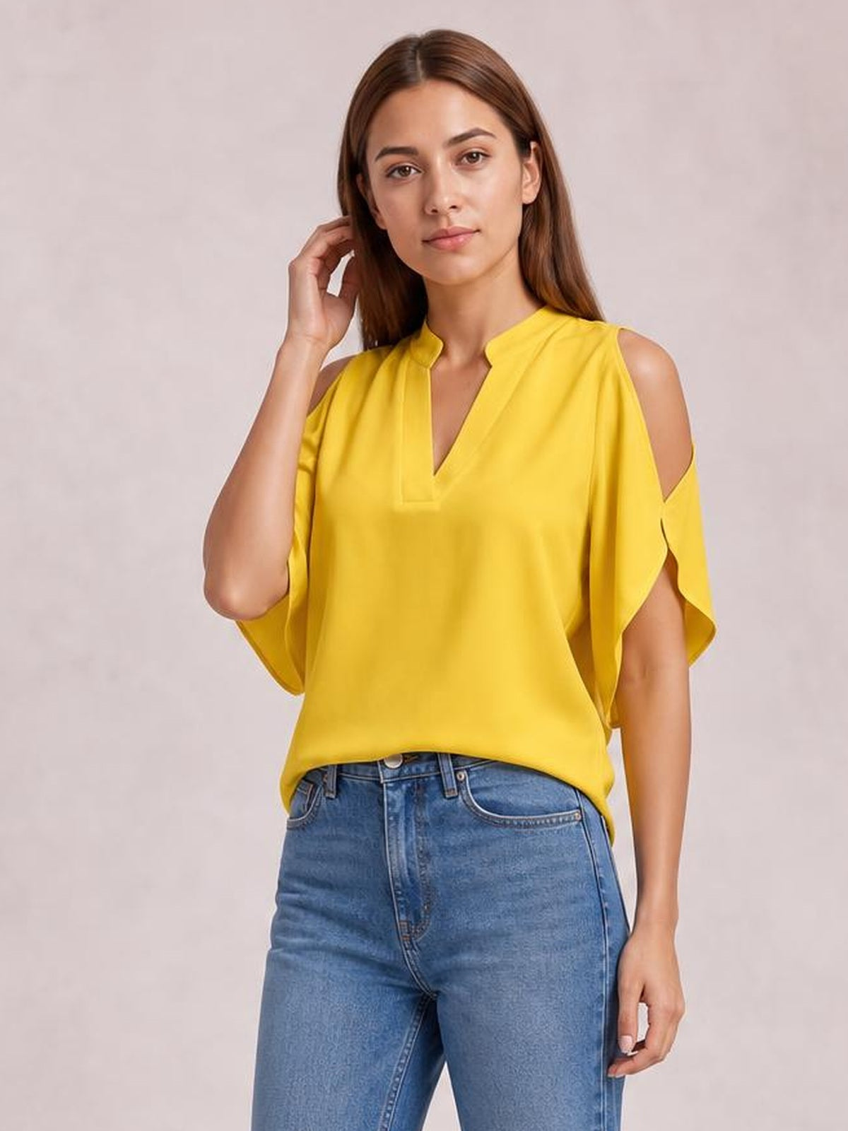 Model touches her hair while wearing a bright yellow notched cold shoulder blouse with a loose silhouette and draped half sleeves.