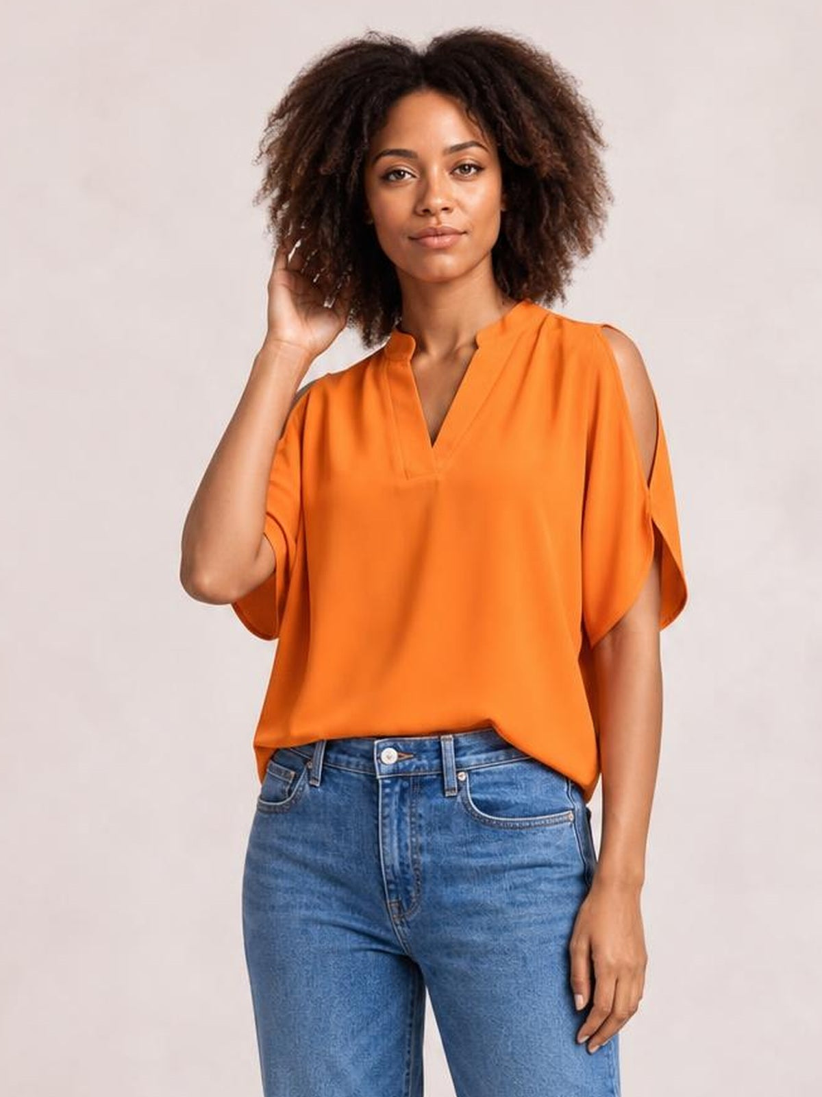 A model poses in a bright orange notched cold shoulder blouse with short half sleeves, shoulder cutouts, a relaxed silhouette, and a softly draped fit.