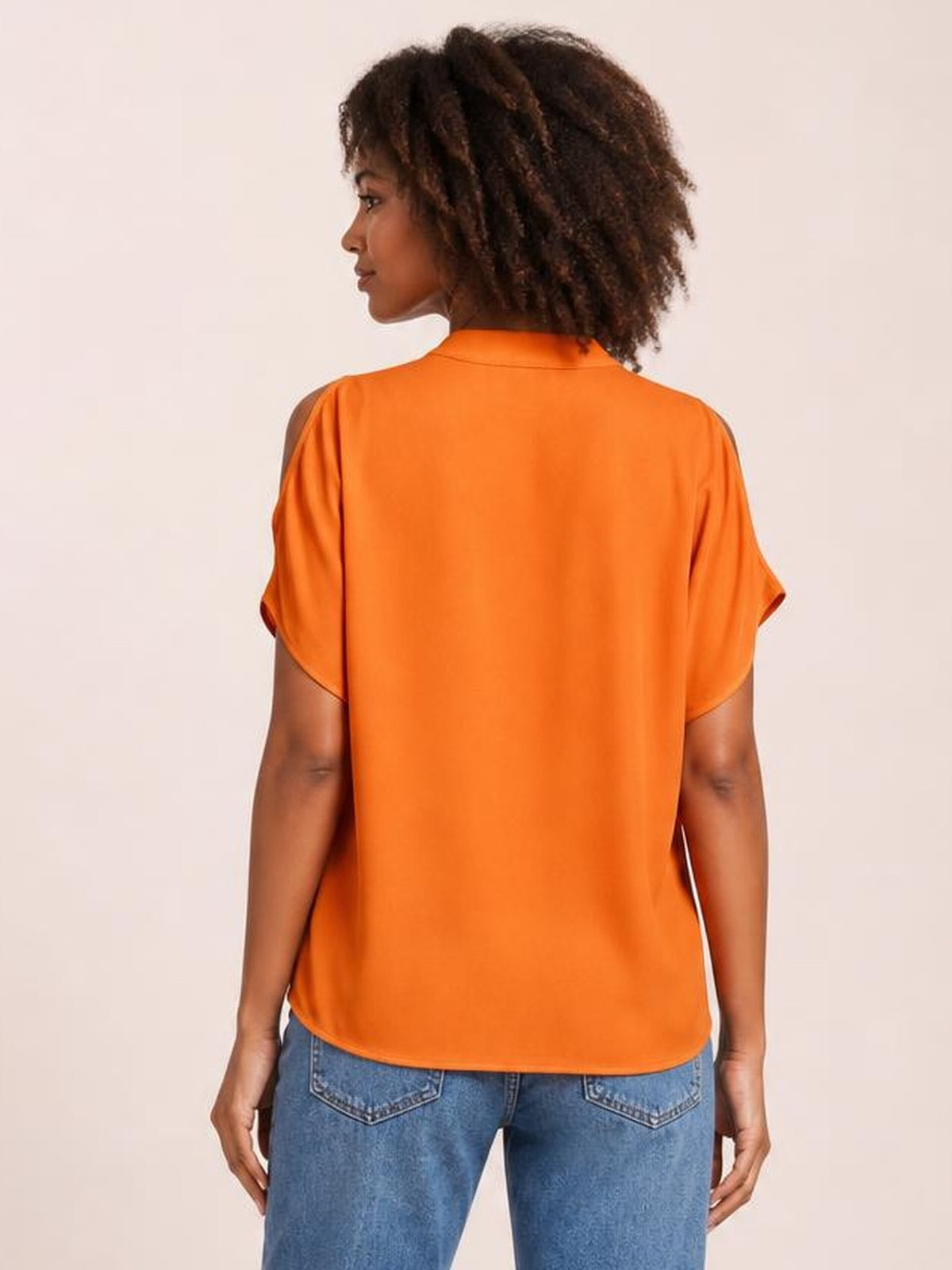 Model shown from behind in a relaxed pose wearing an orange opaque blouse with cold-shoulder cutouts, loose half sleeves, a rounded hem, and a straight silhouette.
