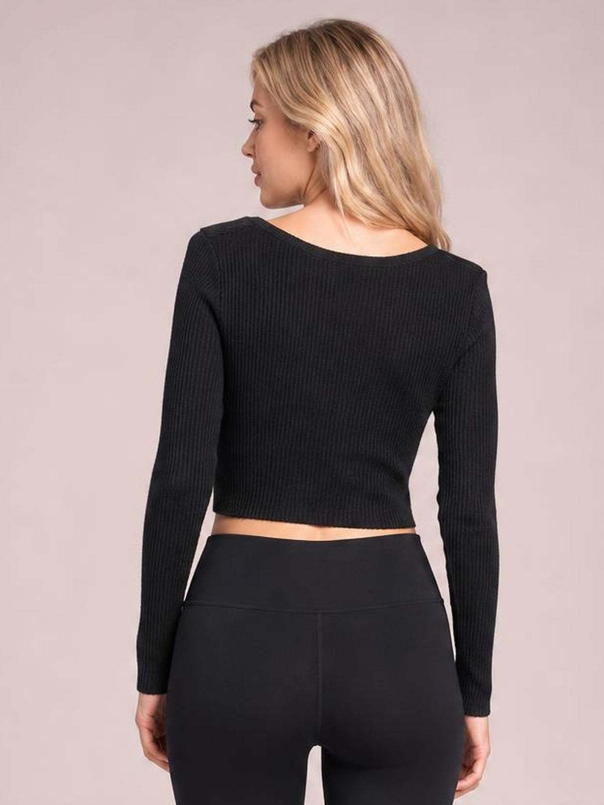 A model stands turned slightly to show the back of a black ribbed long-sleeve T-shirt with a fitted cropped silhouette and wide neckline.