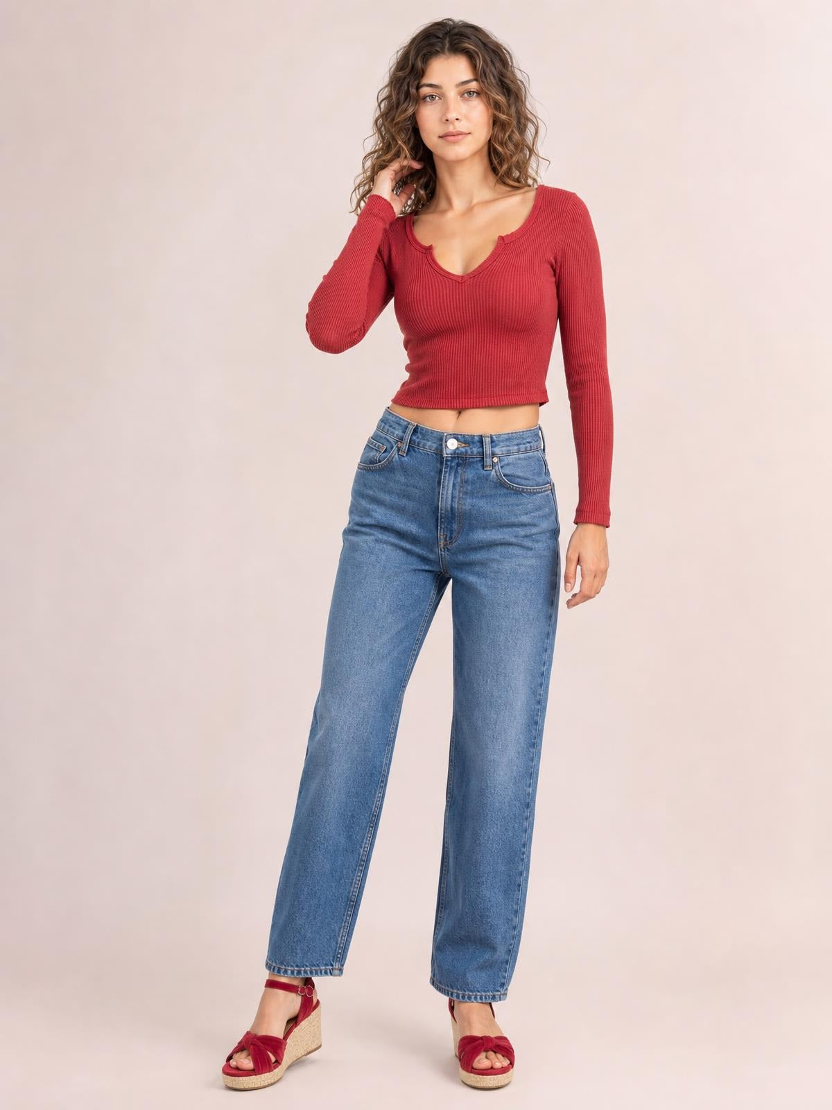 A model poses in a fitted red notched long sleeve T-shirt with ribbed construction and a cropped silhouette, lifting one hand to her hair.