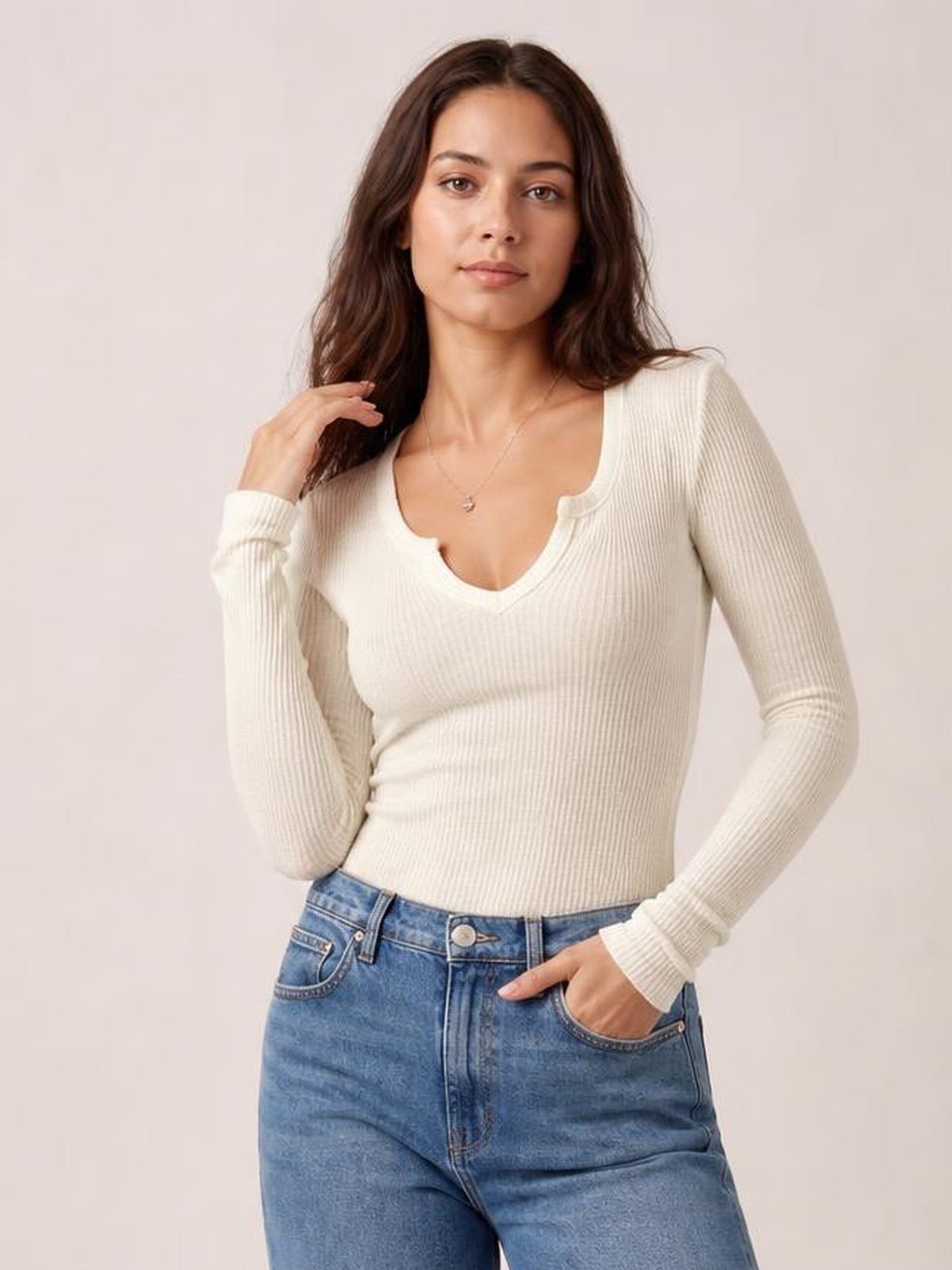 A model poses in a cream notched long sleeve T-shirt with a ribbed texture, fitted silhouette, scoop neckline, and snug cuffs.
