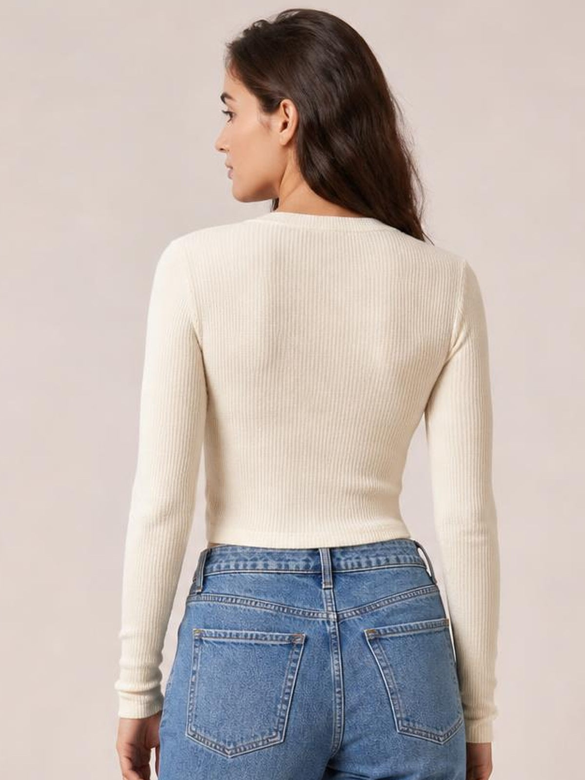 Back view of a model wearing an ivory long sleeve T-shirt with a close-fitting silhouette, fine vertical ribbed texture, and a cropped hem.
