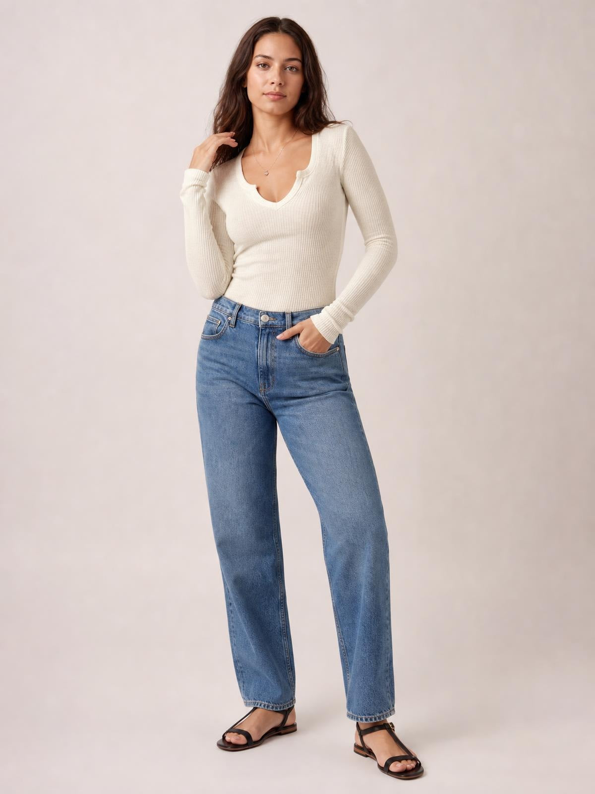 Model wearing an ivory notched long sleeve T-shirt with a fitted ribbed silhouette, standing with one hand in her jeans pocket and the other near her hair.