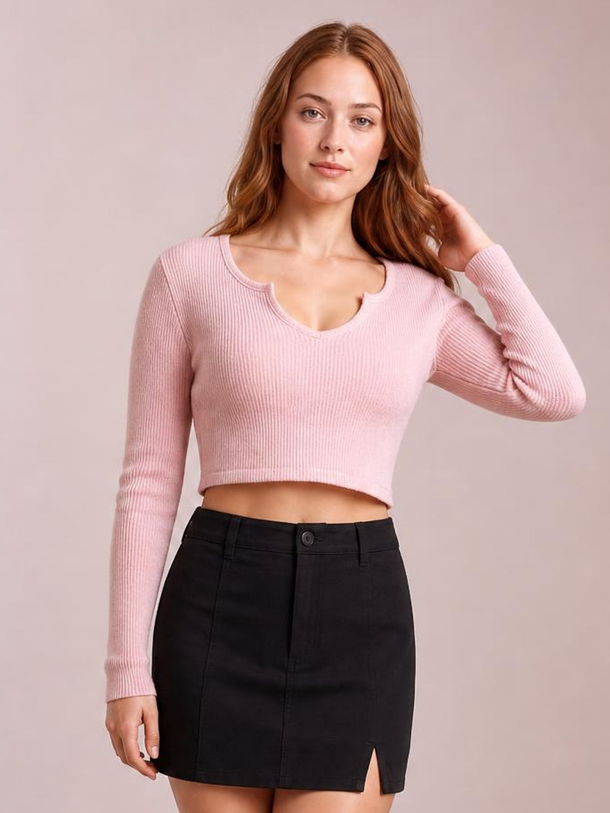 A model poses in a fitted pink ribbed notched long sleeve T-shirt with a cropped silhouette and slightly stretchy construction.