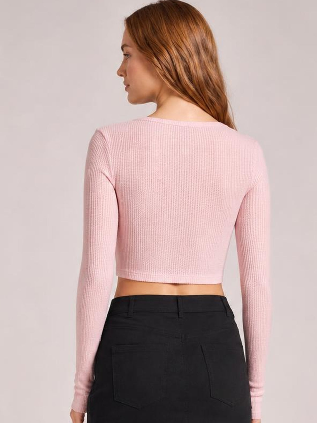 Model shown from behind wearing a light pink notched long sleeve T-shirt with a fitted cropped silhouette and subtly ribbed construction.