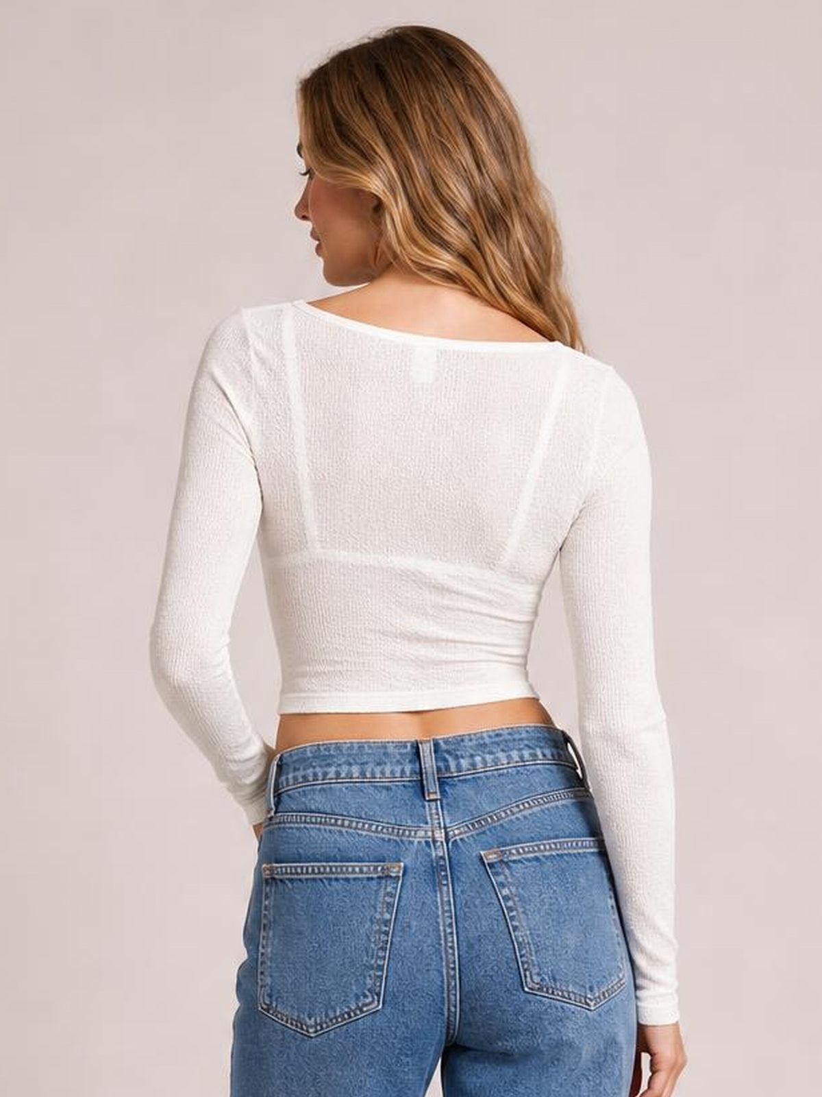 A model poses from behind in a white fitted Notched Long Sleeve T-Shirt with subtle ribbed texture, long sleeves, and a waist-length silhouette.
