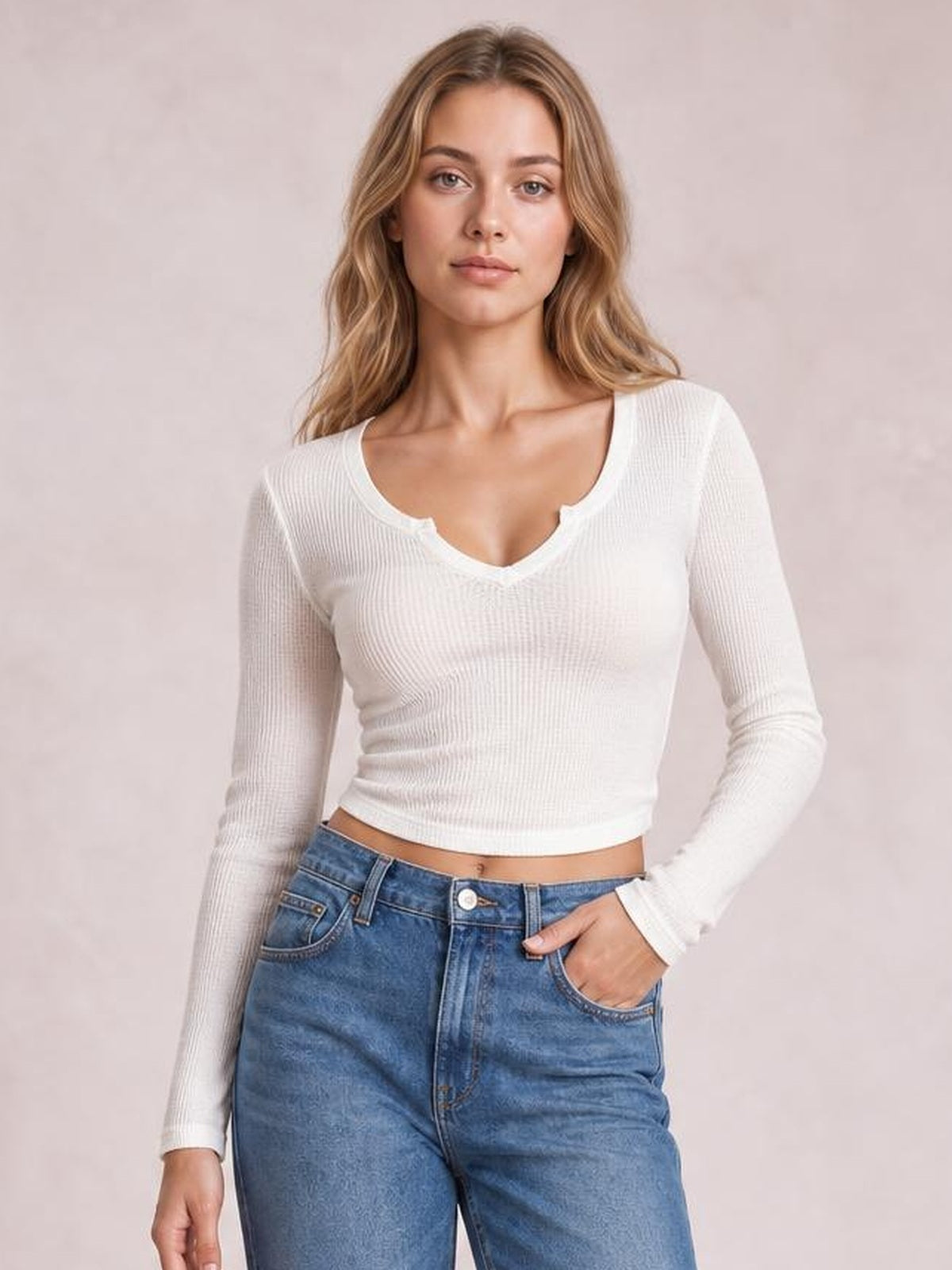 Model wearing a white notched long sleeve T-shirt with a fitted, slightly stretchy ribbed silhouette and cropped hem, posing with one hand in her jeans pocket.