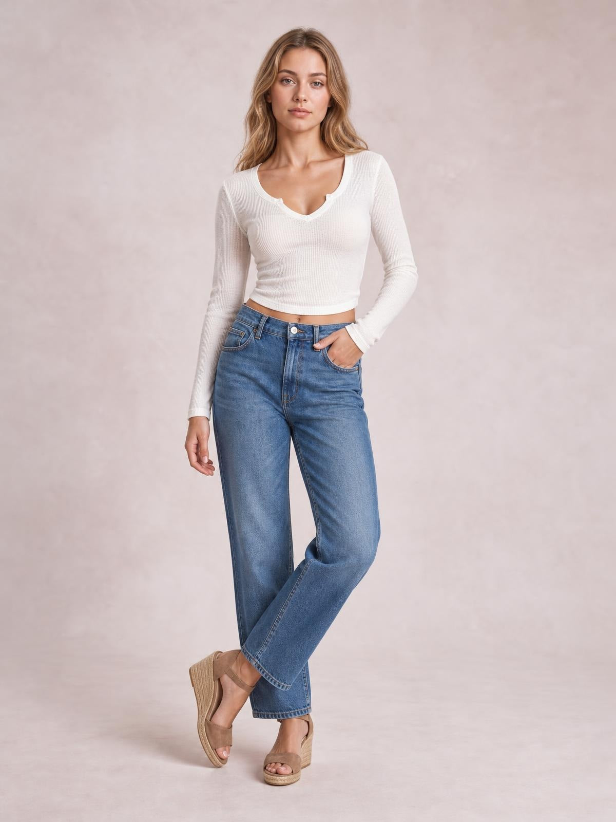 Model poses in a white notched long sleeve T-shirt with a fitted silhouette, ribbed construction, cropped hem, and scoop neckline.