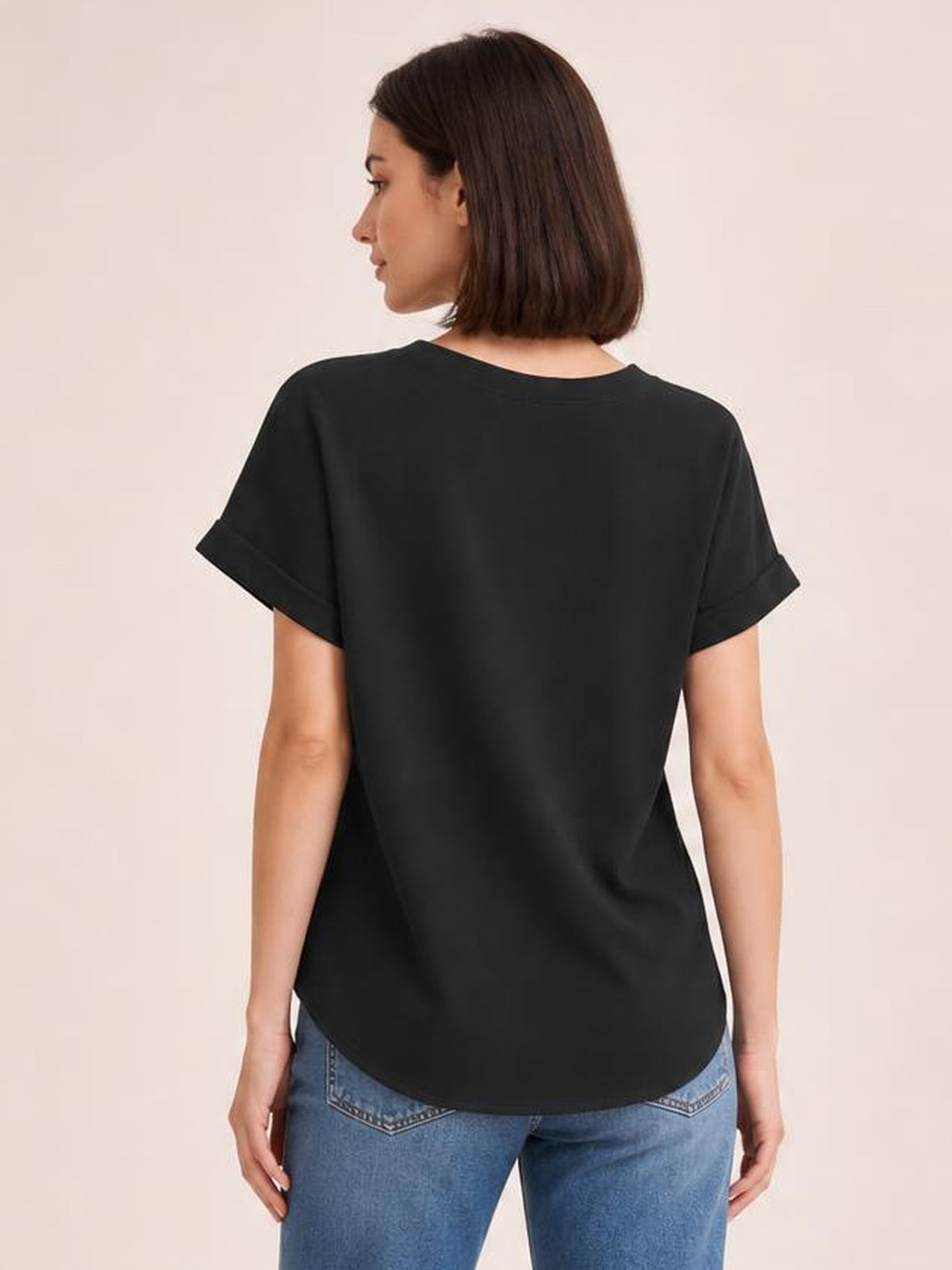 A model stands in a black solid shirt with short cuffed sleeves, a relaxed regular-length silhouette, and a softly curved hem, viewed from the back.