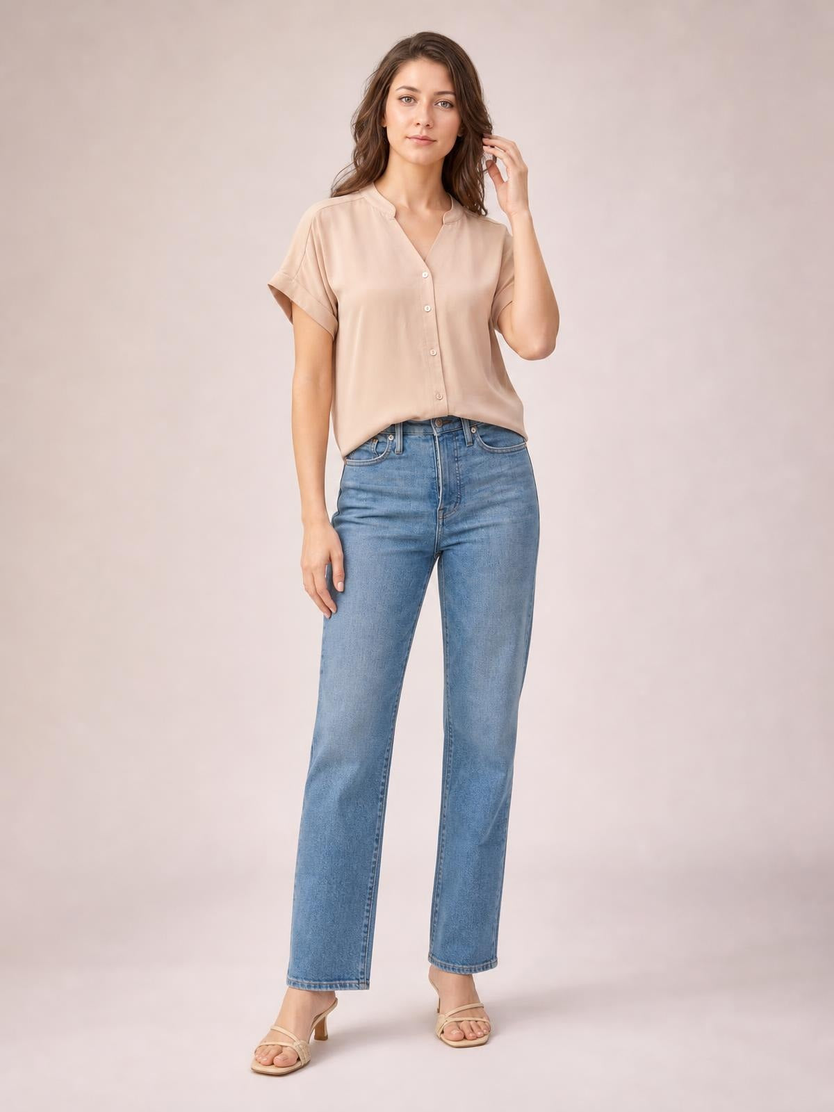 Model wears a solid beige notched-neck shirt with button front, cuffed short sleeves, and a relaxed regular-length silhouette while touching her hair.