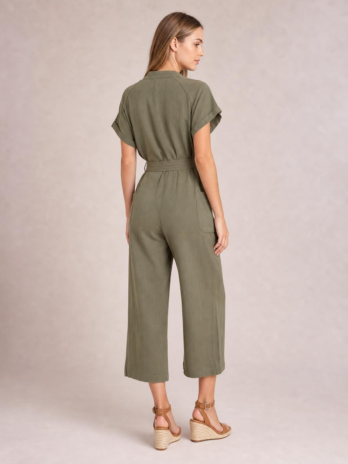 Model shown from behind in an olive short-sleeve jumpsuit with cuffed sleeves, a tied waist, wide cropped legs, and practical back pockets.