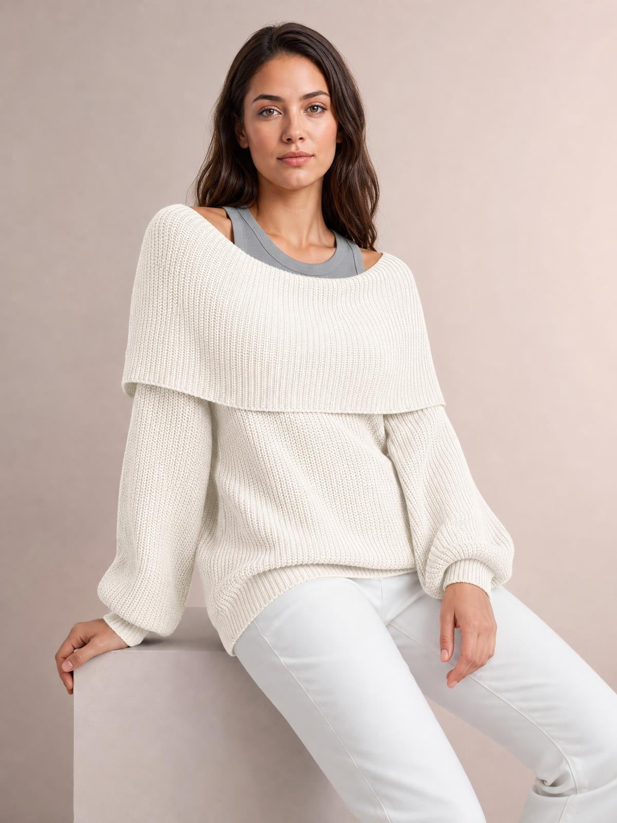 Model seated in an oversized ivory ribbed off-shoulder sweater with long balloon sleeves, wide neckline, and relaxed silhouette.