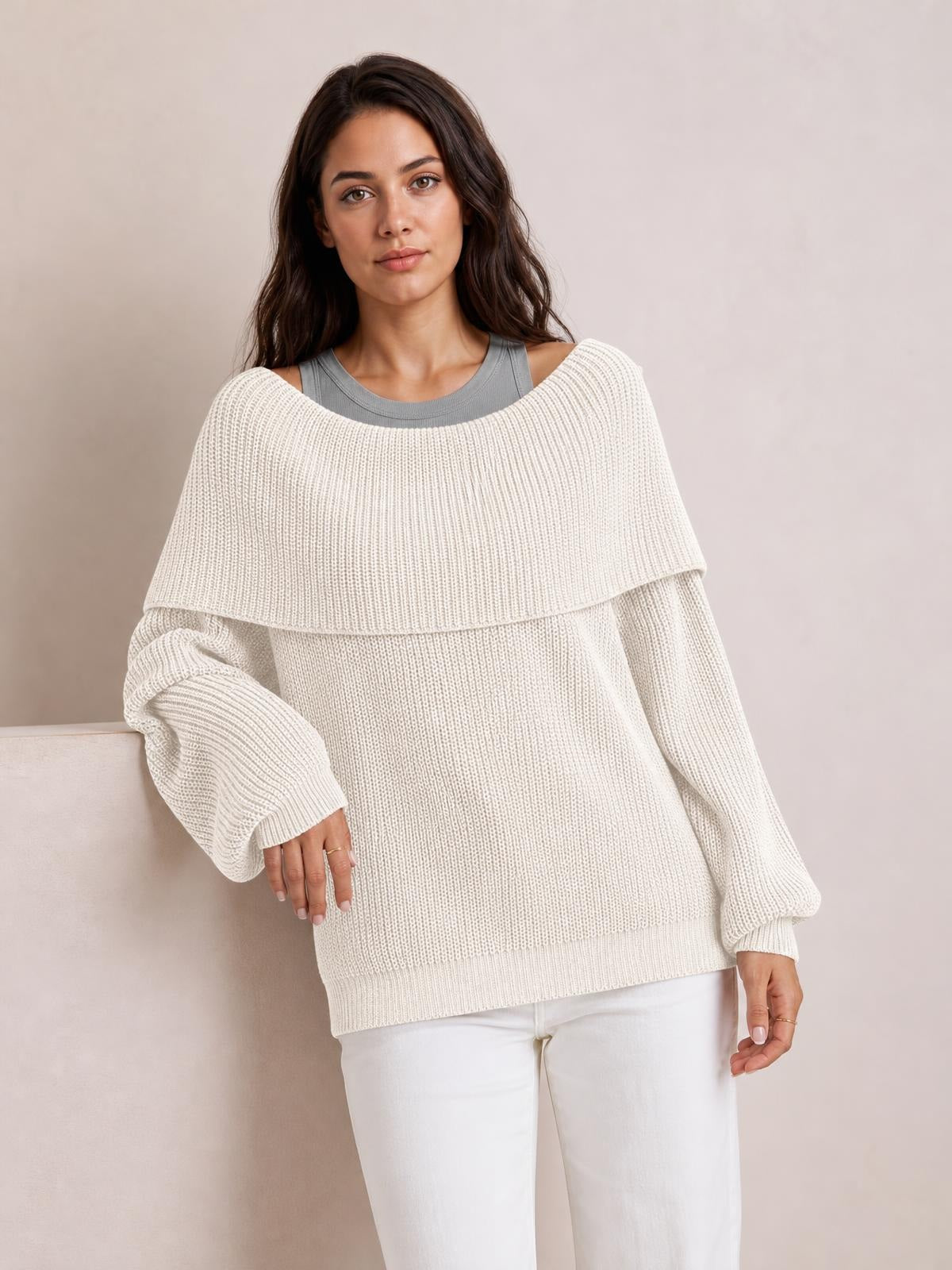 Model wears an oversized ivory off-shoulder long sleeve sweater with ribbed knit construction, wide neckline, relaxed silhouette, and ribbed cuffs and hem.