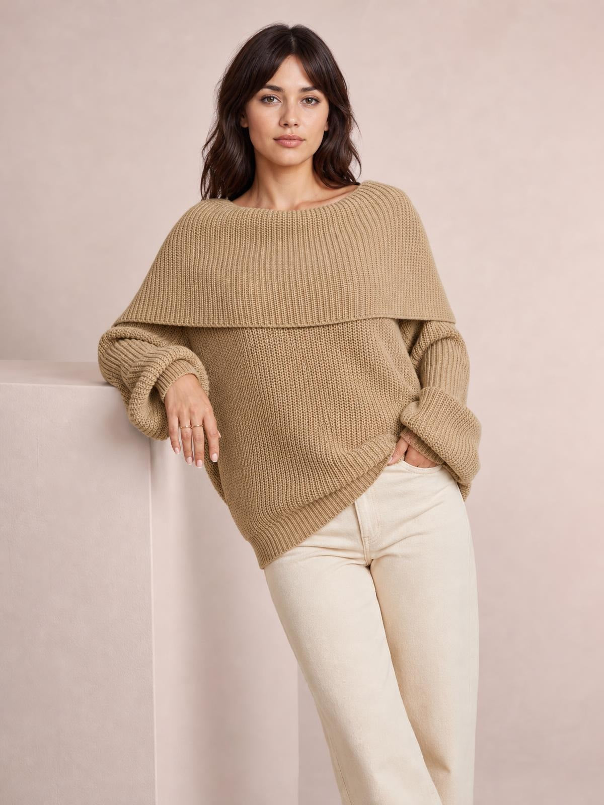 A model poses in a taupe oversized ribbed off-shoulder long sleeve sweater with a wide neckline, relaxed silhouette, dropped sleeves, and ribbed cuffs and hem.