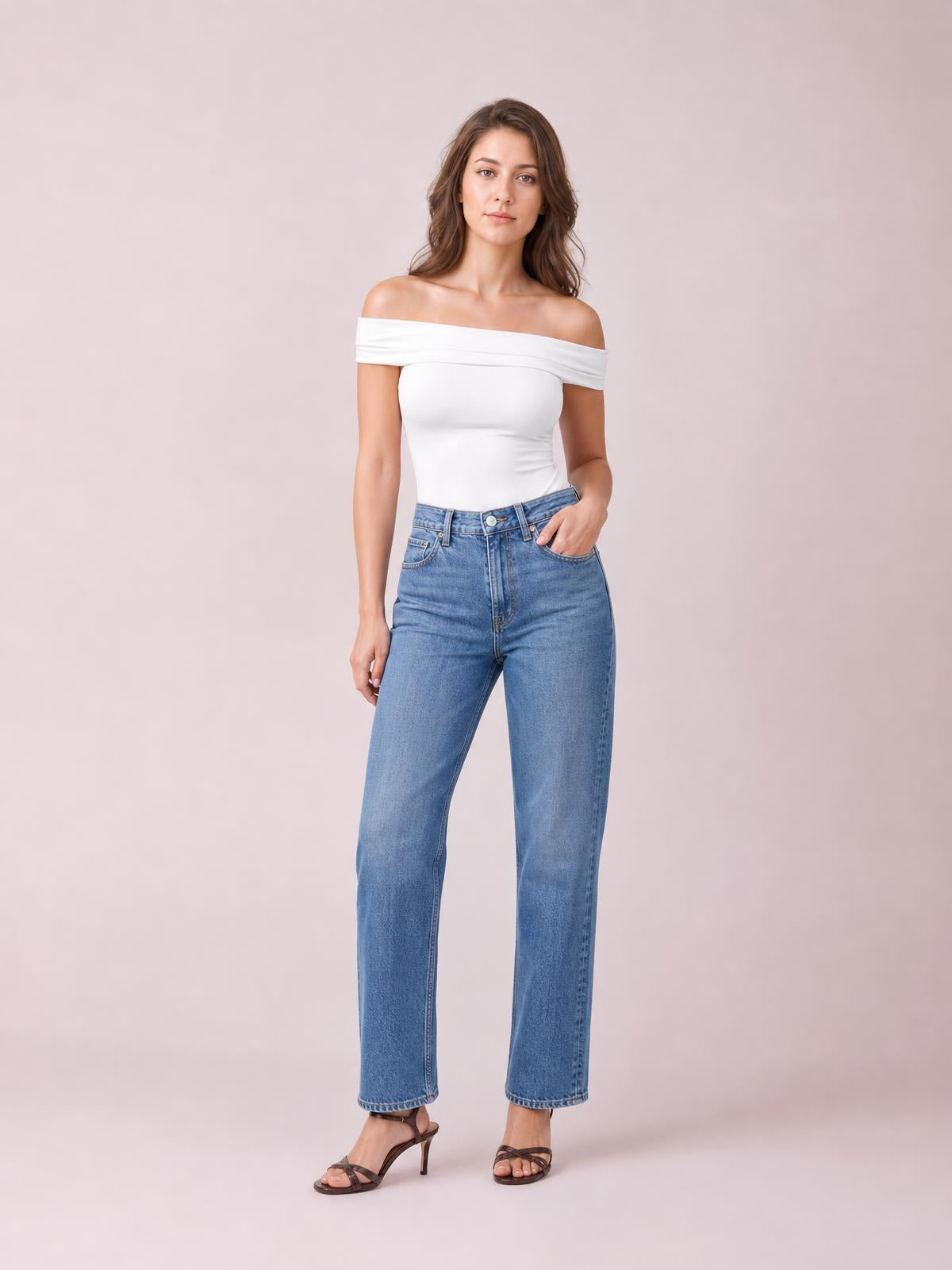 Model poses in a white off-shoulder short sleeve blouse with a fitted silhouette and folded neckline, paired with straight-leg blue jeans.