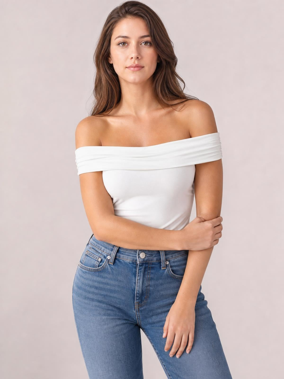 Model wearing a white off-shoulder short sleeve blouse with a fitted silhouette and wide folded neckline, standing with one arm crossed.