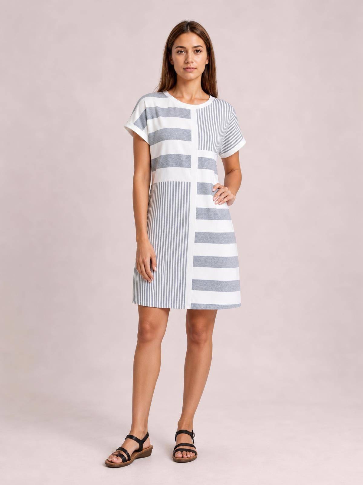 Model poses in a white and gray striped round-neck mini tee dress with short sleeves, a straight relaxed silhouette, and mixed horizontal and vertical stripes.