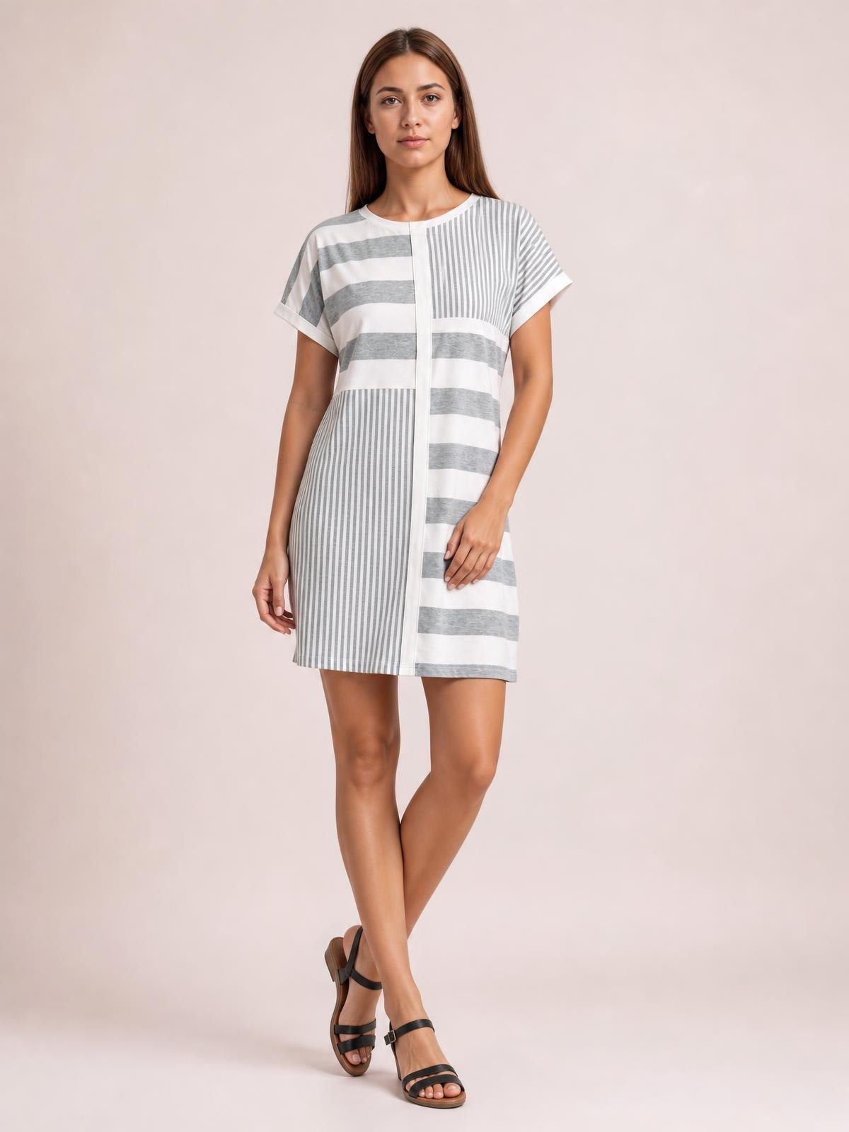 Model stands with crossed legs in a white and gray striped round-neck short-sleeve mini tee dress with a straight silhouette and mixed horizontal and vertical stripes.