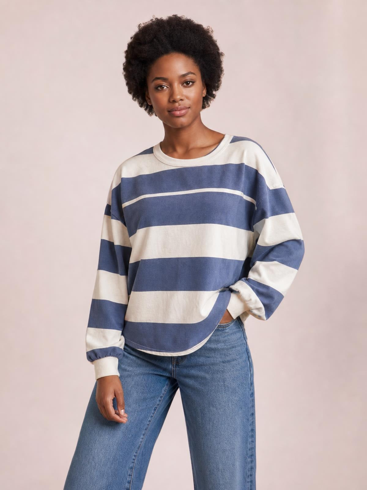 A model poses in a relaxed blue and ivory contrast striped round-neck long-sleeve T-shirt with exposed seams and a loose silhouette.