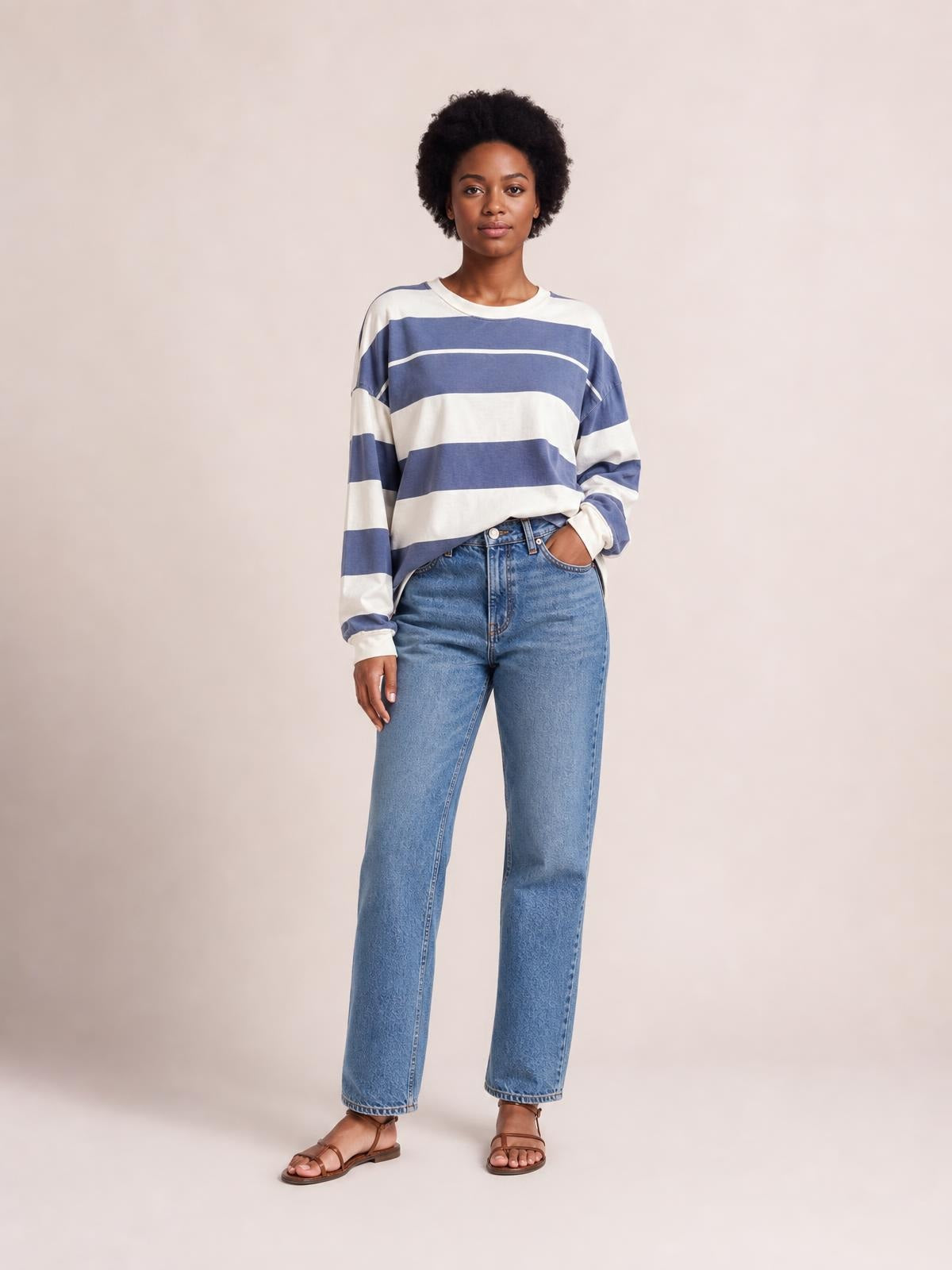 Model wearing a relaxed blue and white contrast striped round-neck long-sleeve T-shirt with exposed seams and a loose silhouette, one hand in her jeans pocket.