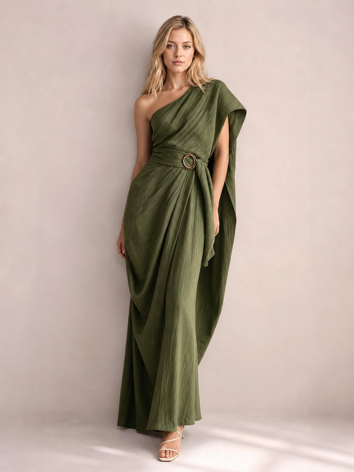 Model wears an olive green one-shoulder draped maxi dress with a flowing floor-length silhouette, gathered waist, and circular buckle detail.