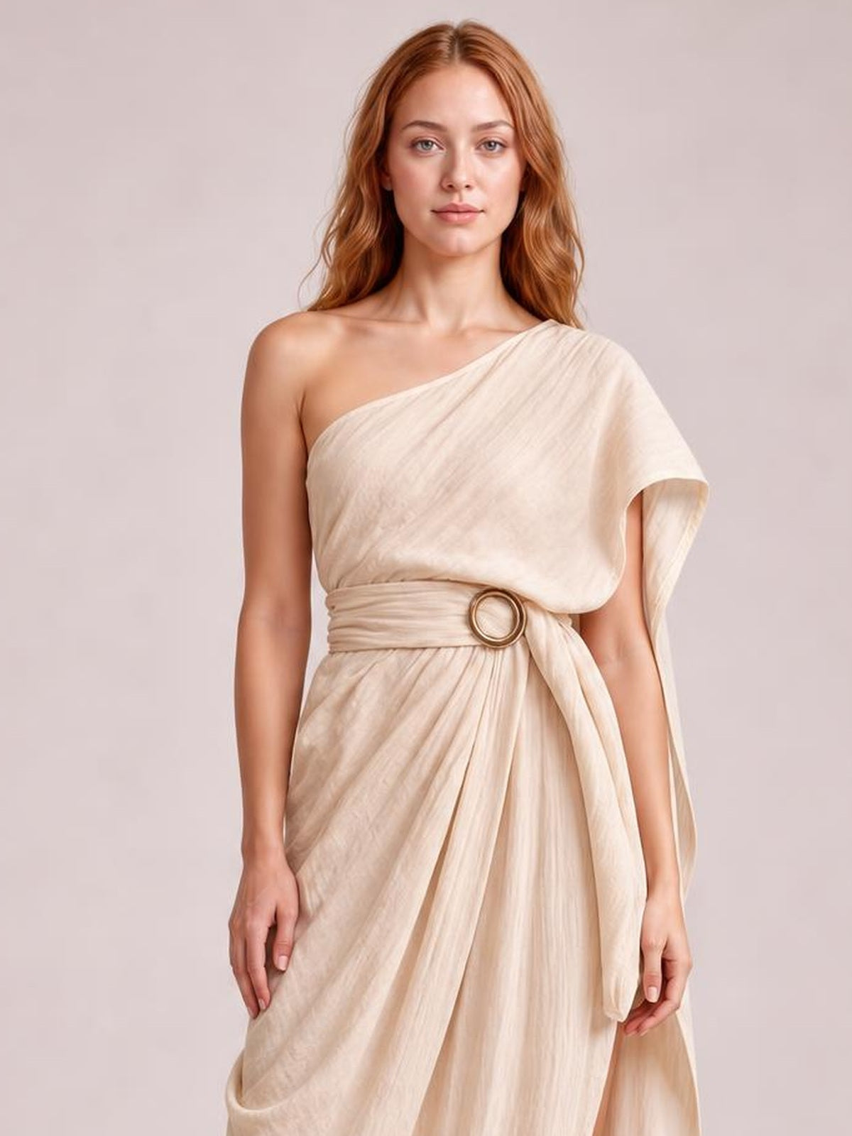 A model stands in a cream one-shoulder draped maxi dress with a flowing silhouette, gathered waist, and wide sash finished with a circular buckle.