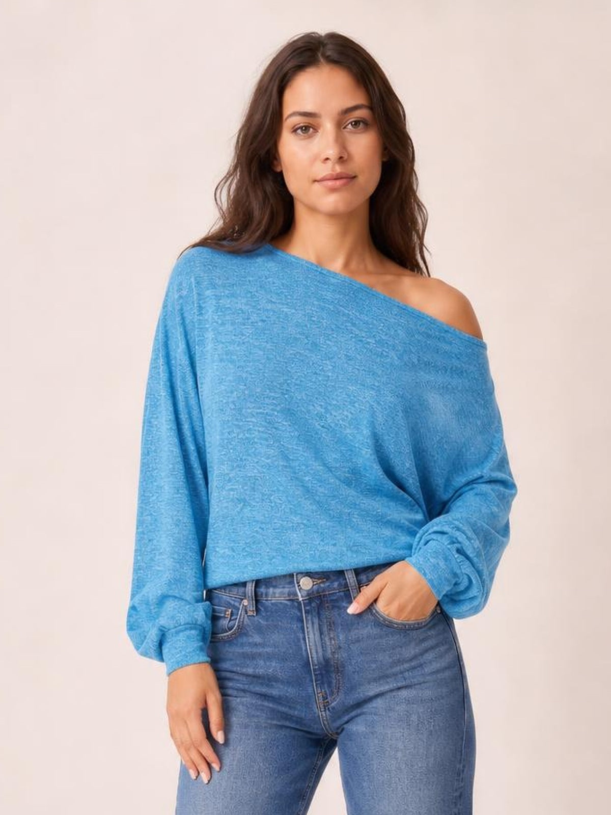 Model wears a blue one-shoulder long-sleeve T-shirt with a relaxed silhouette, exposed shoulder, gathered cuffs, and a decorative button at the waist.