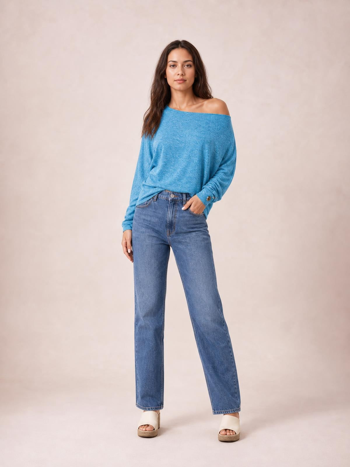 Model poses in a relaxed stance wearing a blue one-shoulder long-sleeve T-shirt with a loose silhouette, gathered cuffs, and decorative button detail.