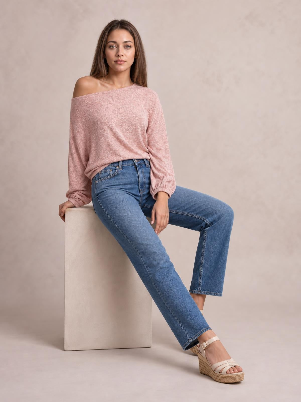 Model seated in a relaxed pose wears a dusty pink one-shoulder long-sleeve T-shirt with a loose silhouette and gathered cuffs.