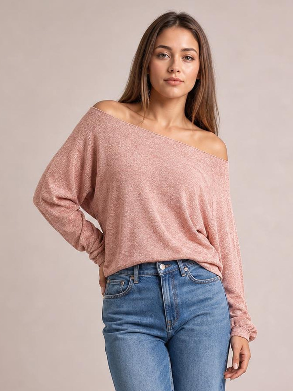Model poses with one hand on her hip wearing a dusty pink one-shoulder long-sleeve T-shirt with a relaxed silhouette and wide neckline.