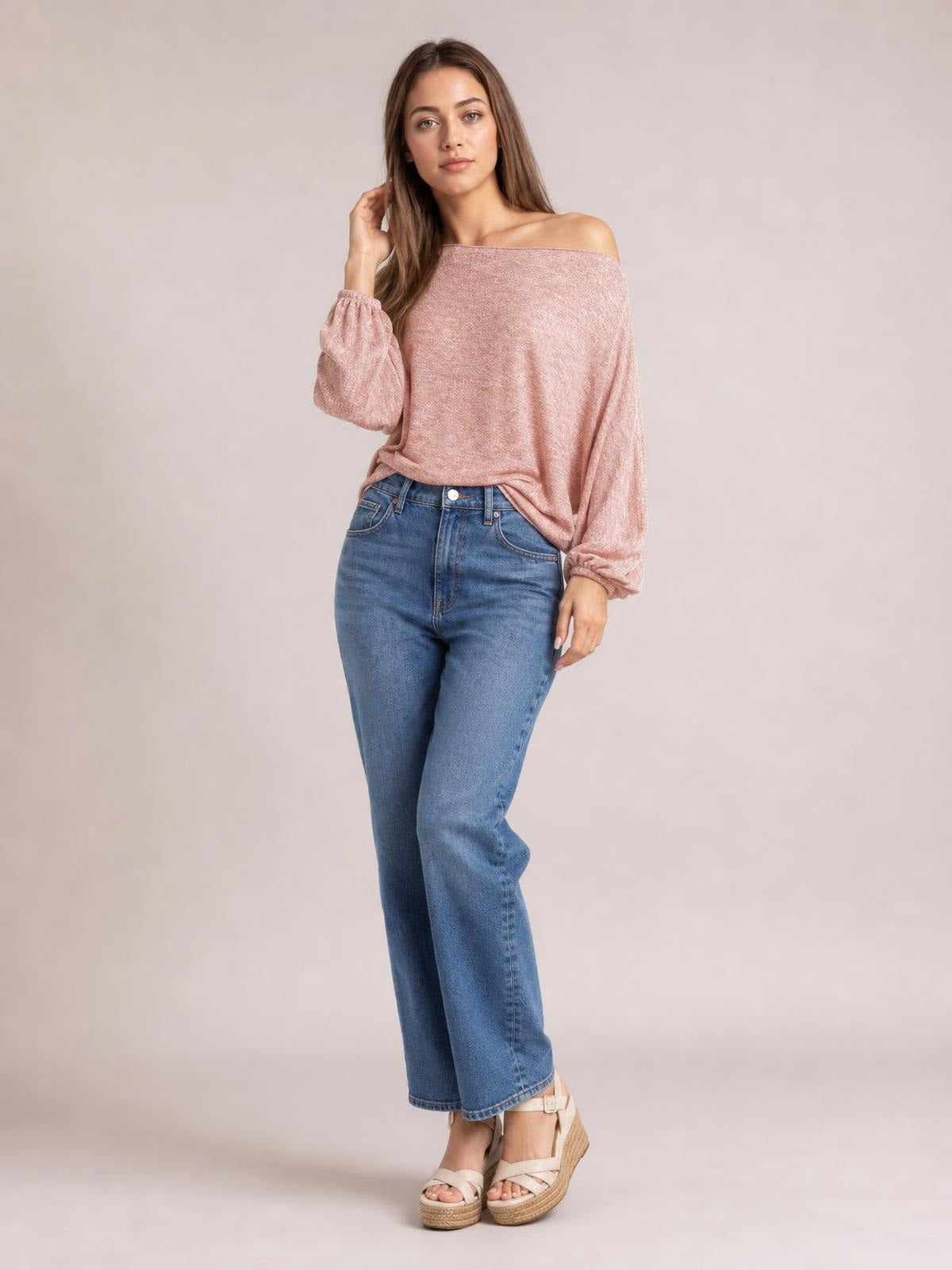 Model poses in a pink one-shoulder long-sleeve T-shirt with gathered cuffs and a relaxed draped silhouette, paired with blue jeans.
