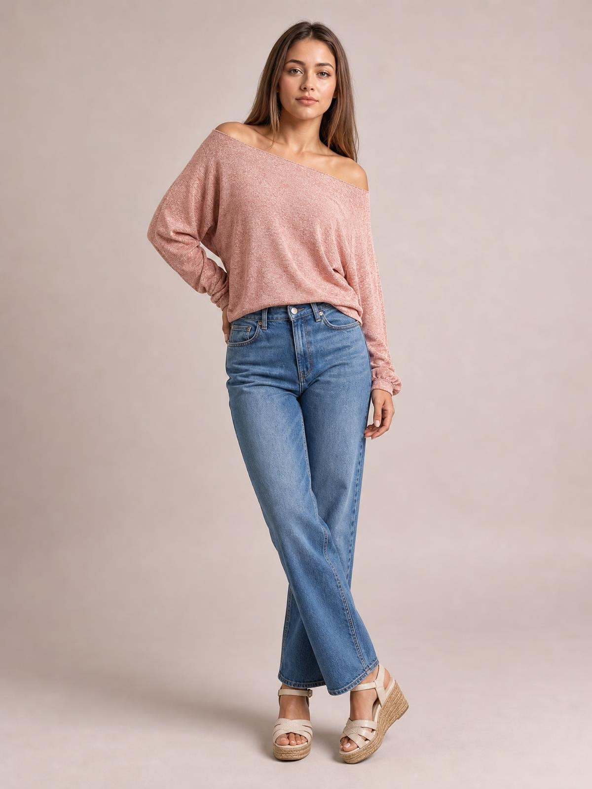 A model poses in a dusty rose one-shoulder long-sleeve T-shirt with a relaxed draped silhouette and slightly gathered cuffs, paired with jeans.