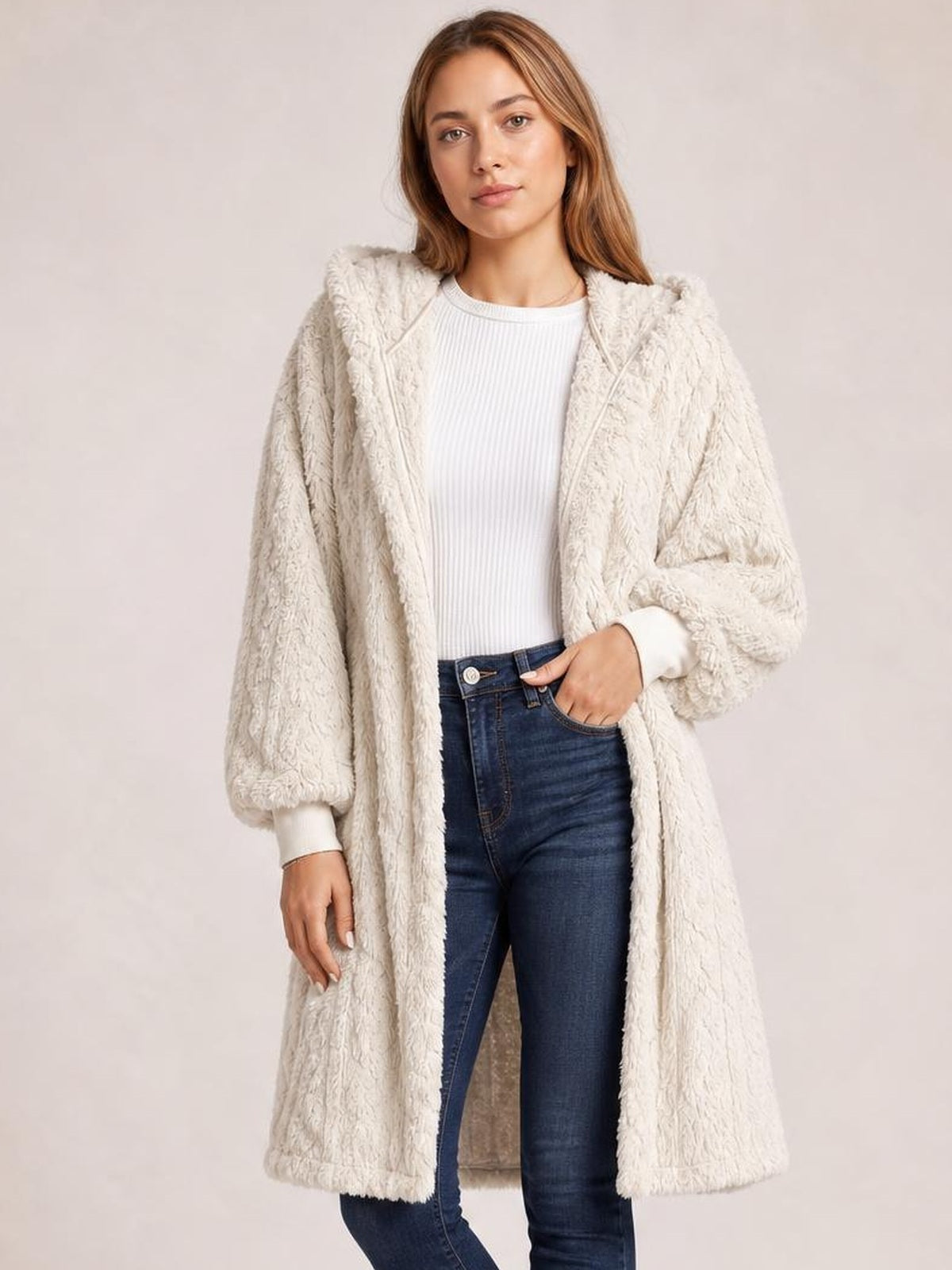 A model stands with one hand in her jeans pocket wearing a cream fuzzy hooded jacket with an open front, long sleeves, and a long relaxed silhouette.