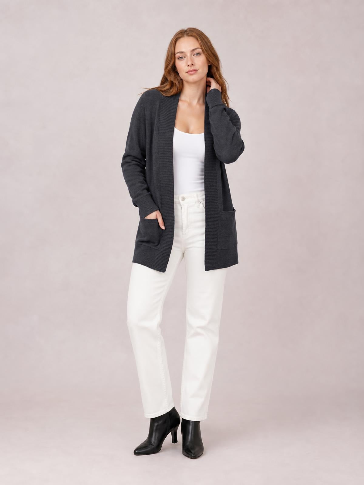Model wearing a charcoal open-front long-sleeve sweater cardigan with ribbed trim, relaxed long silhouette, and front pockets over a white top.
