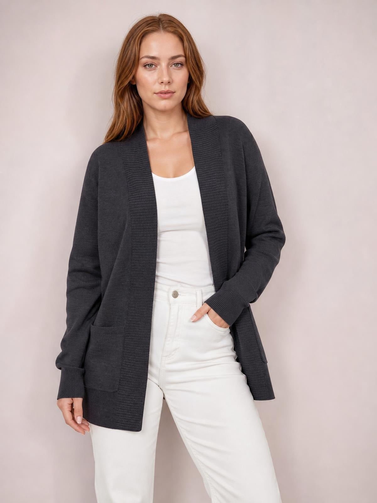 Model wearing a charcoal open front long sleeve sweater cardigan with ribbed trim, relaxed long silhouette, and front pockets, posing with one hand in a pocket.