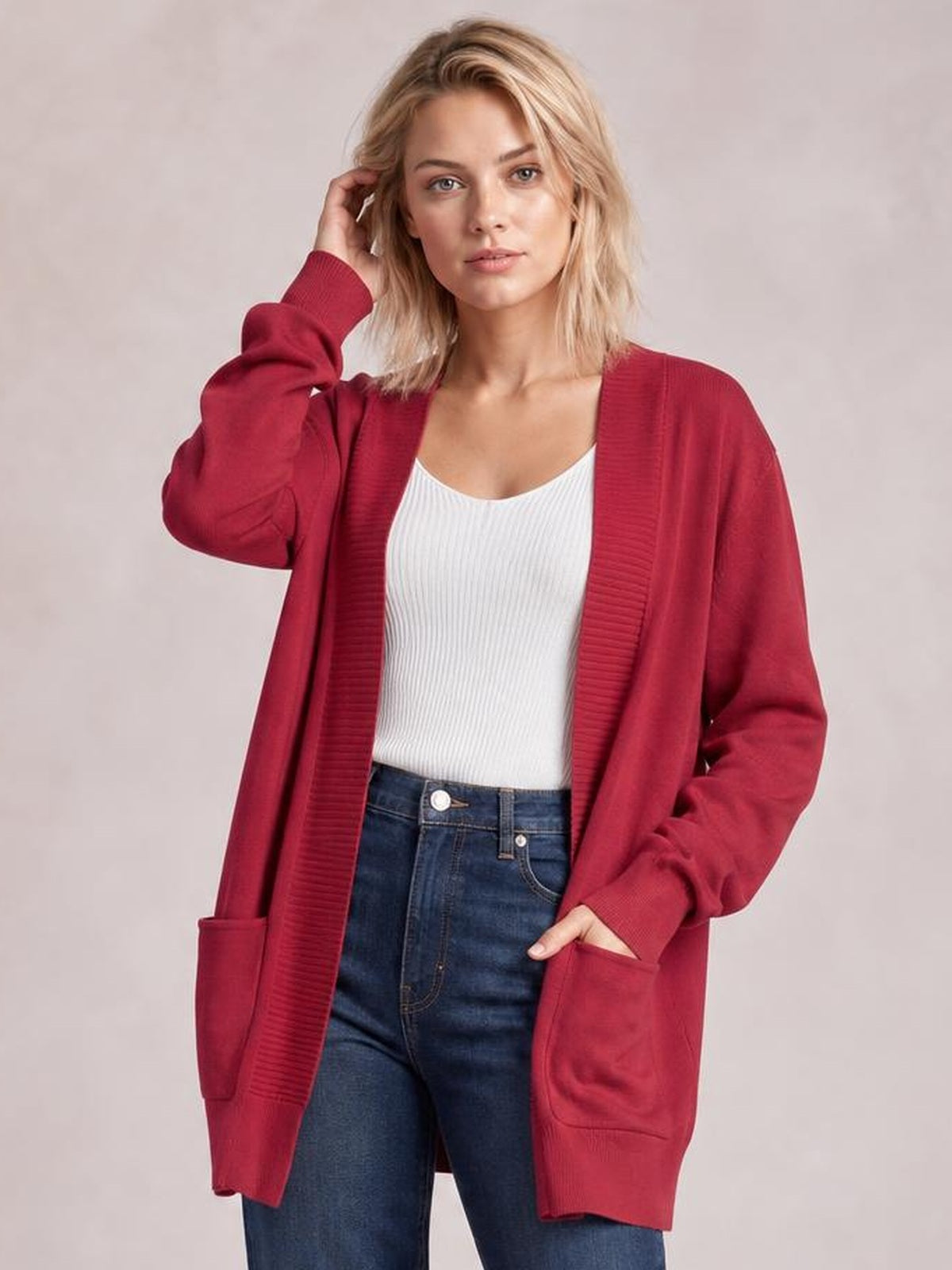 Model wears a burgundy open-front long-sleeve sweater cardigan with a relaxed long silhouette, ribbed trim, and two patch pockets over a white top.