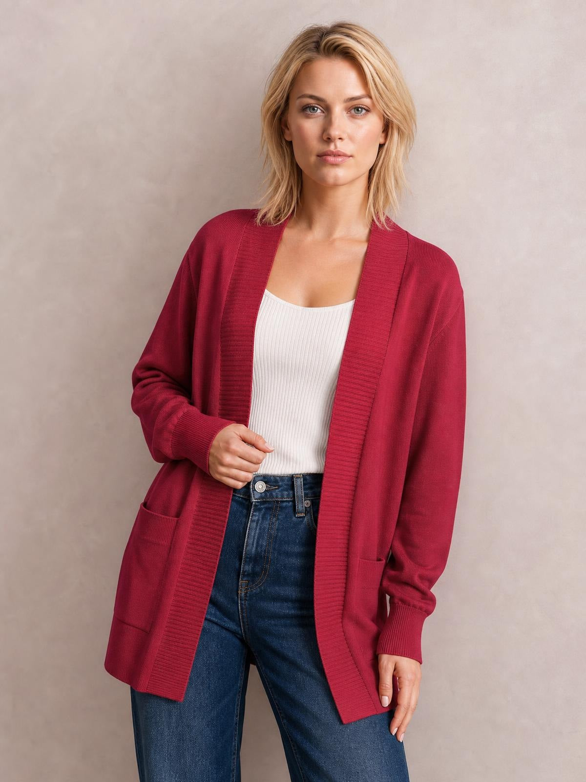 Model wearing a burgundy open front long sleeve sweater cardigan with ribbed trim, relaxed silhouette, and front pockets over a white top.