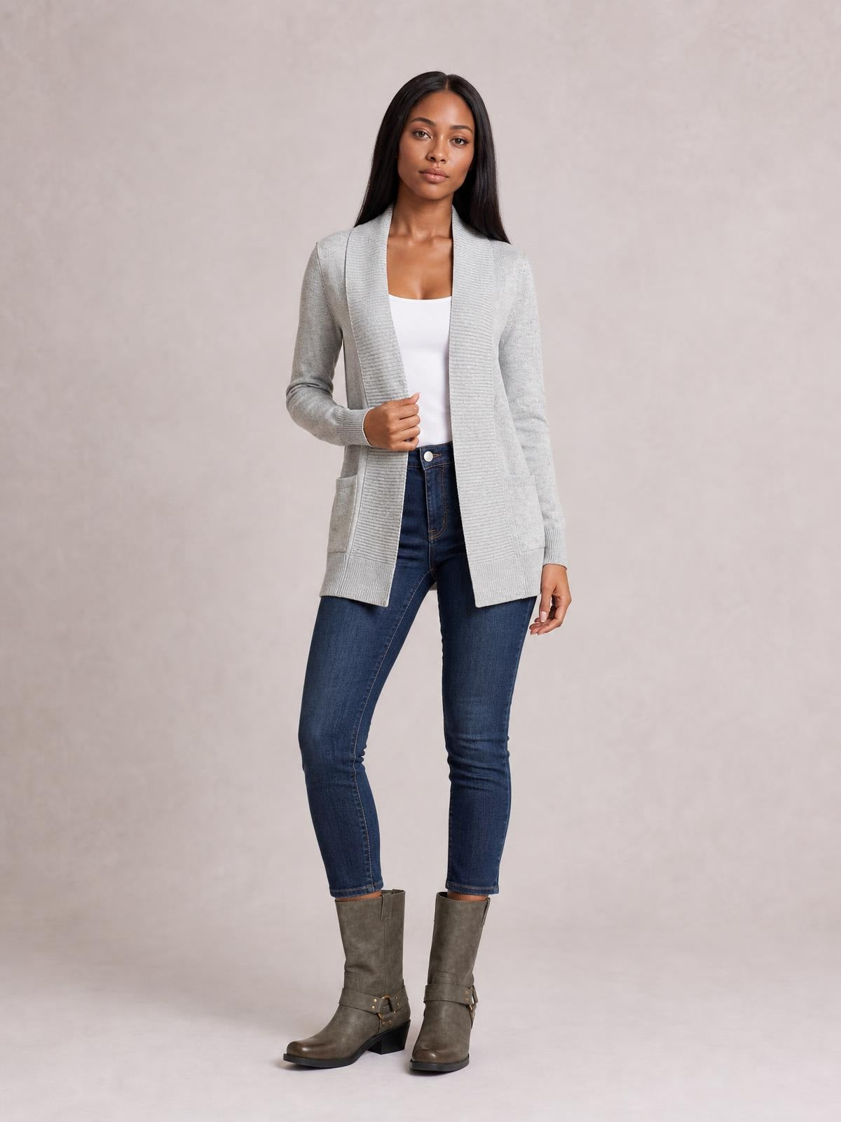 A model wears a light gray open front long sleeve sweater cardigan with a long silhouette, ribbed trim, and front pockets over a white top.