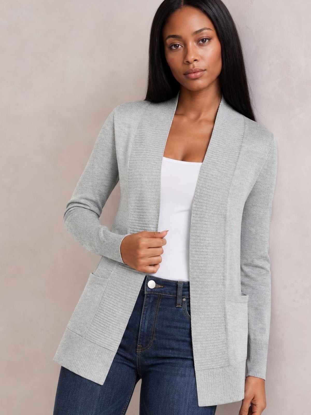 Model wearing a light gray open-front long-sleeve sweater cardigan with ribbed cuffs, front pockets, and a long relaxed silhouette over a white top.