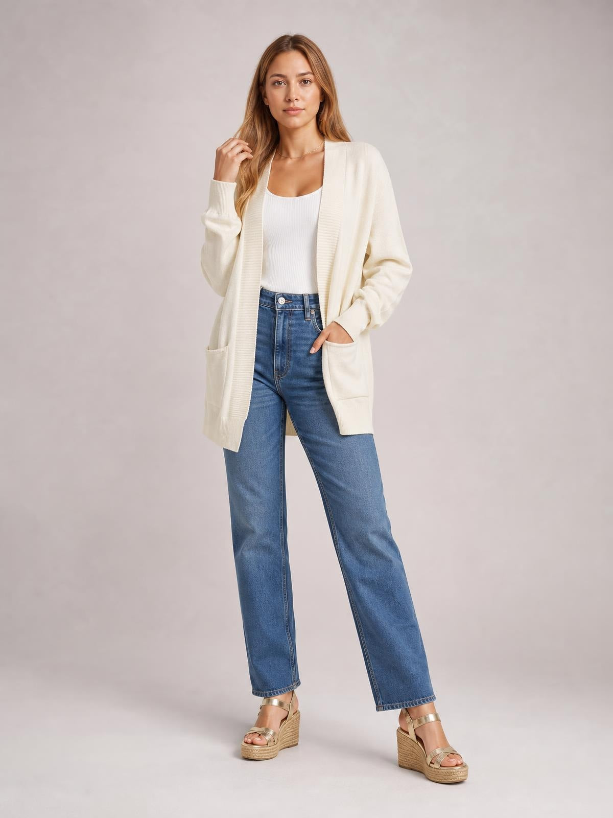Model wears an ivory open front long sleeve sweater cardigan with a relaxed longline silhouette, ribbed trim, and two front pockets.